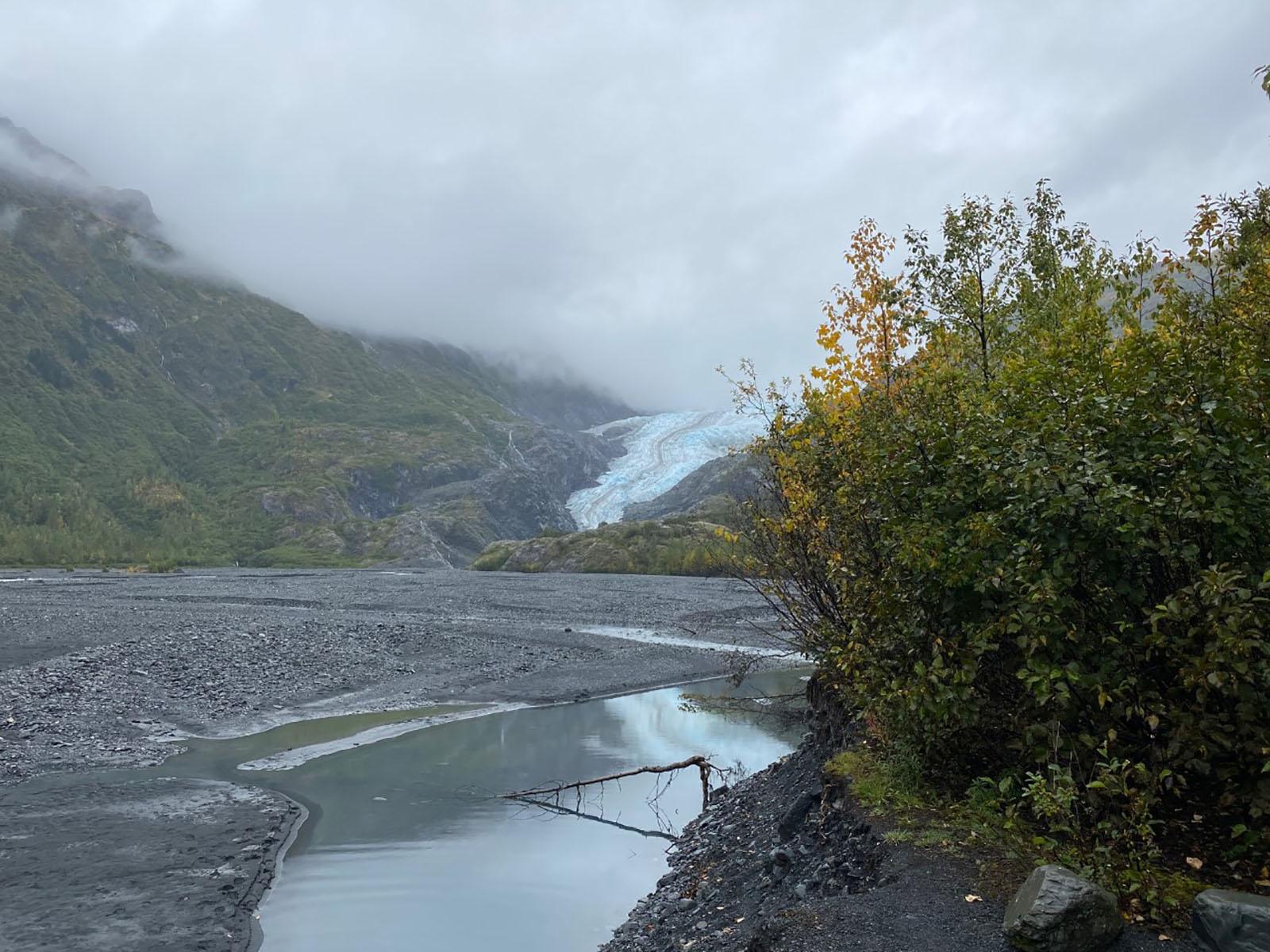 A glacier flowing between two plant covered mountainsides in the distance.