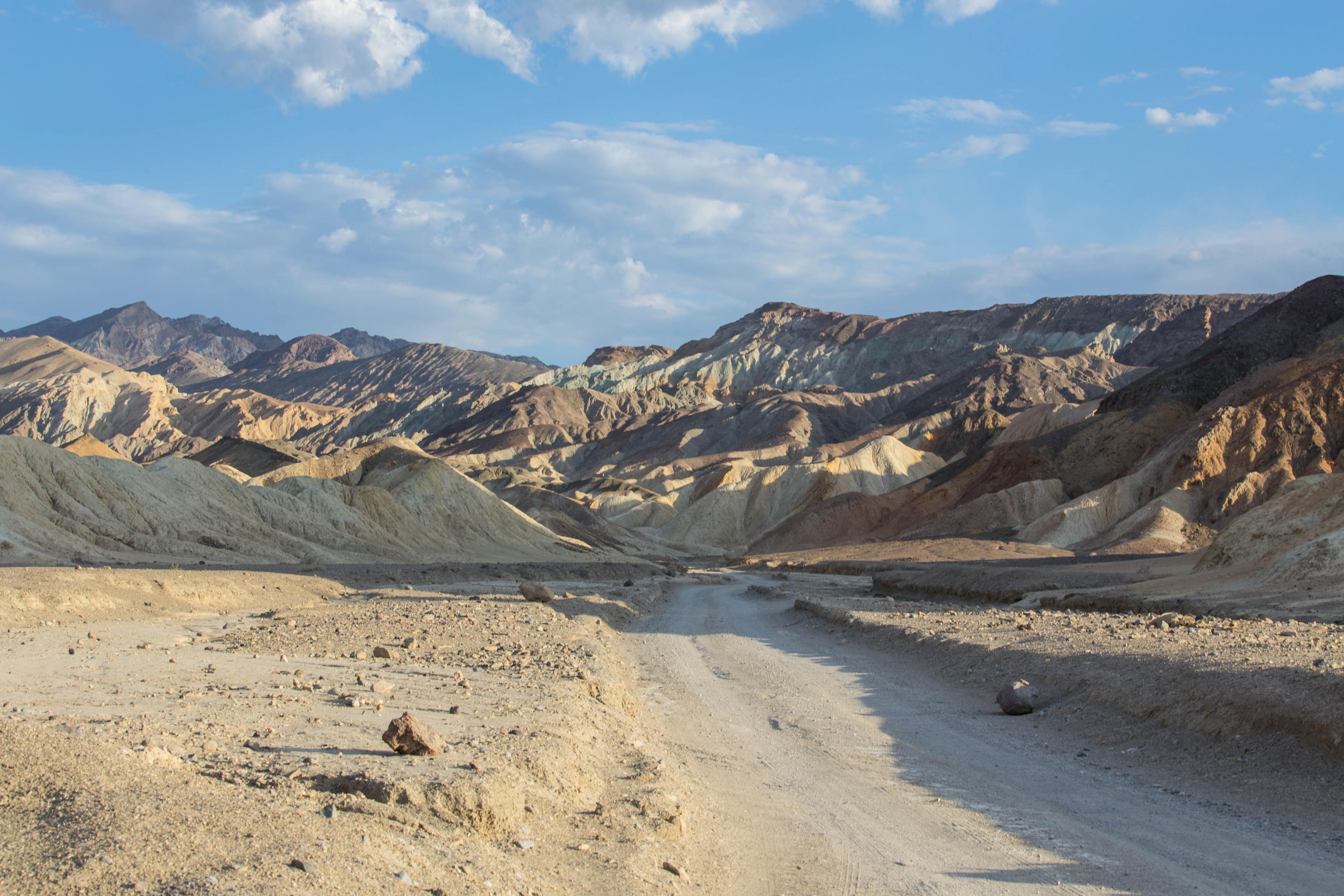 A dirt road through bare brown and yellow striped hills.