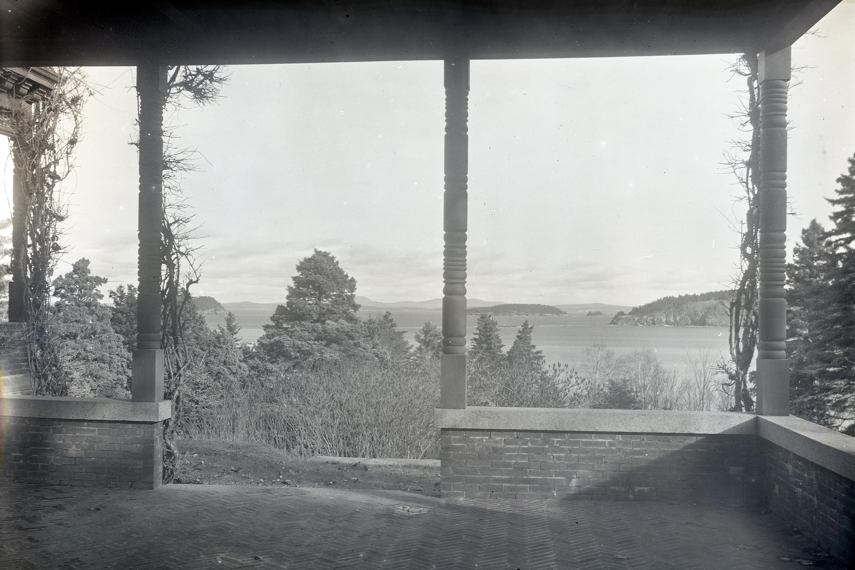 View from a covered patio across trees in foreground of a harbor and islands in the distance.