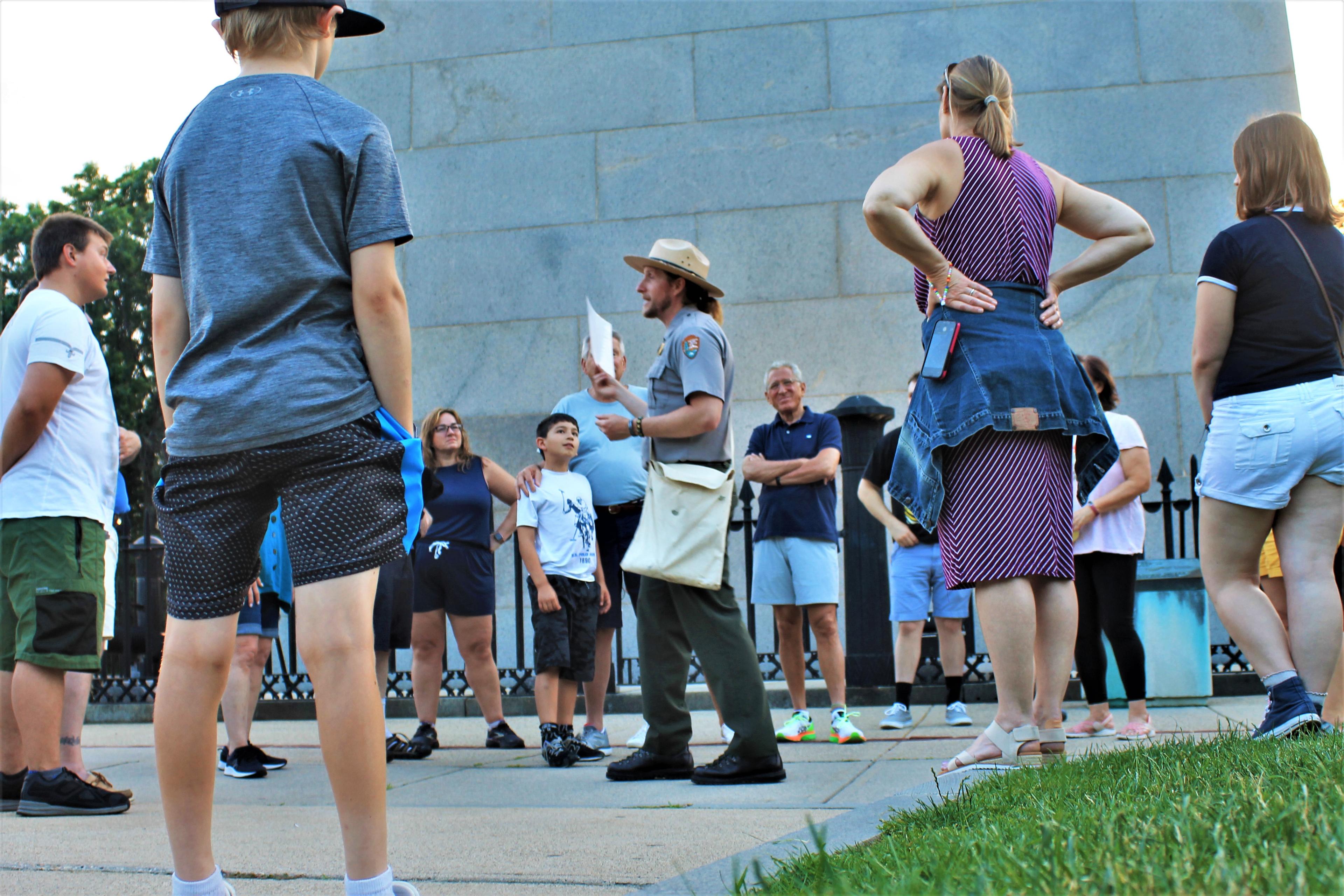 Ranger speaking in front of the Bunker Hill Monument to a group that surrounds him in a circle.