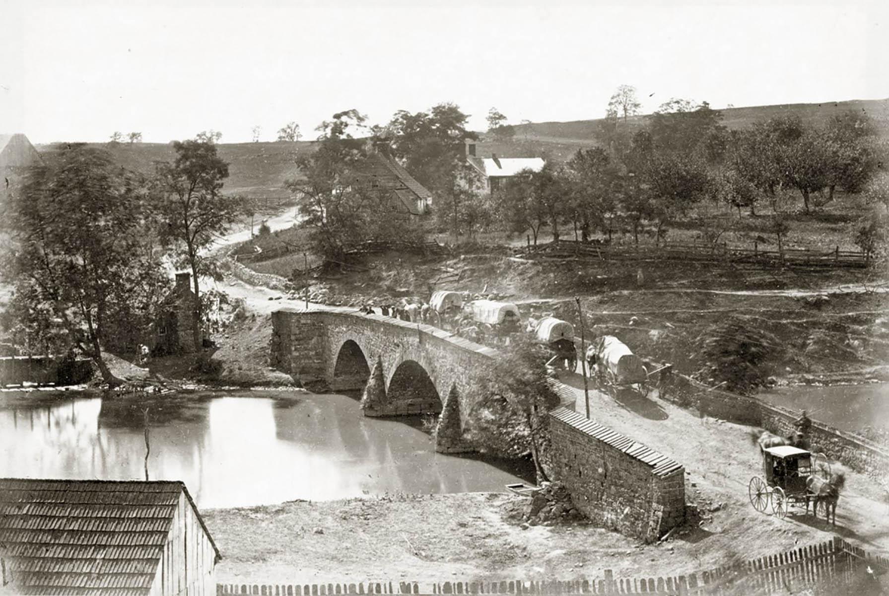 black and white photo of a stone bridge over a creek