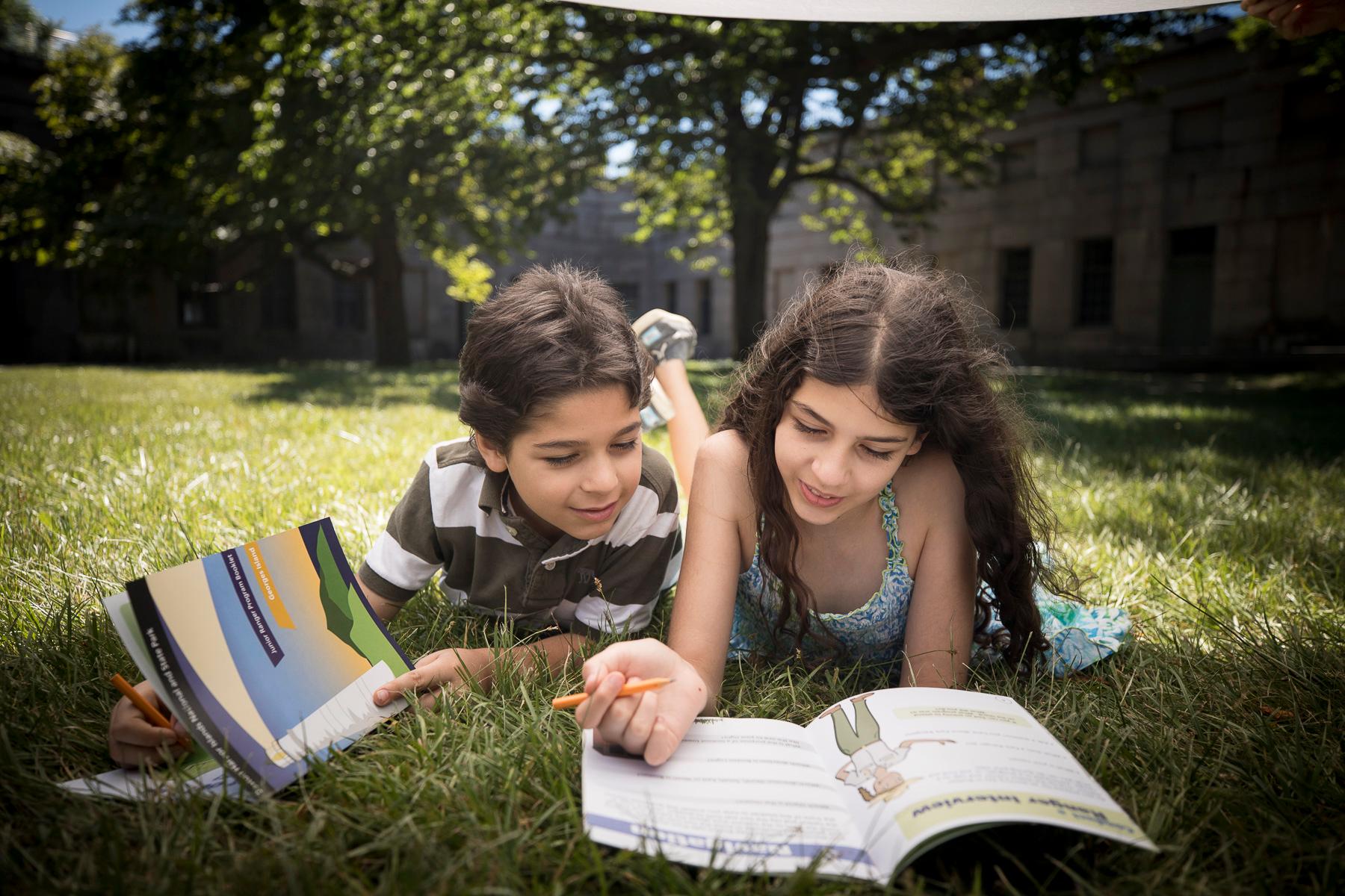 A boy and a girl lying on the grass working on junior ranger books.