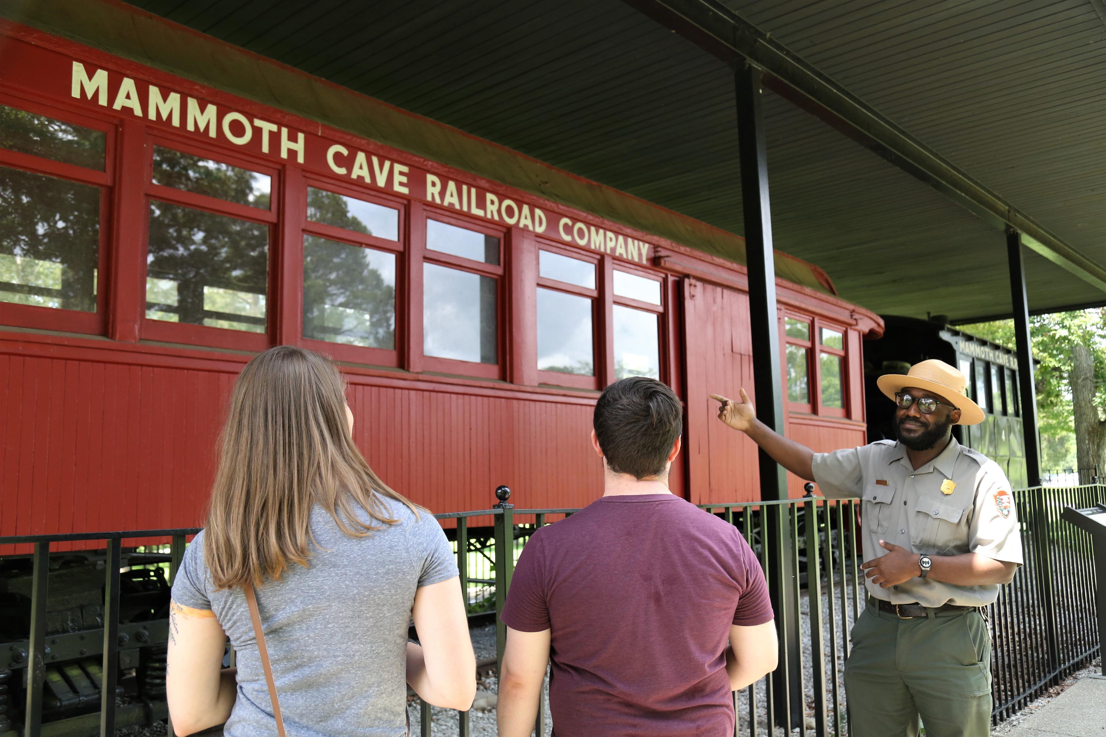 A ranger talks to two park visitors near a historic train