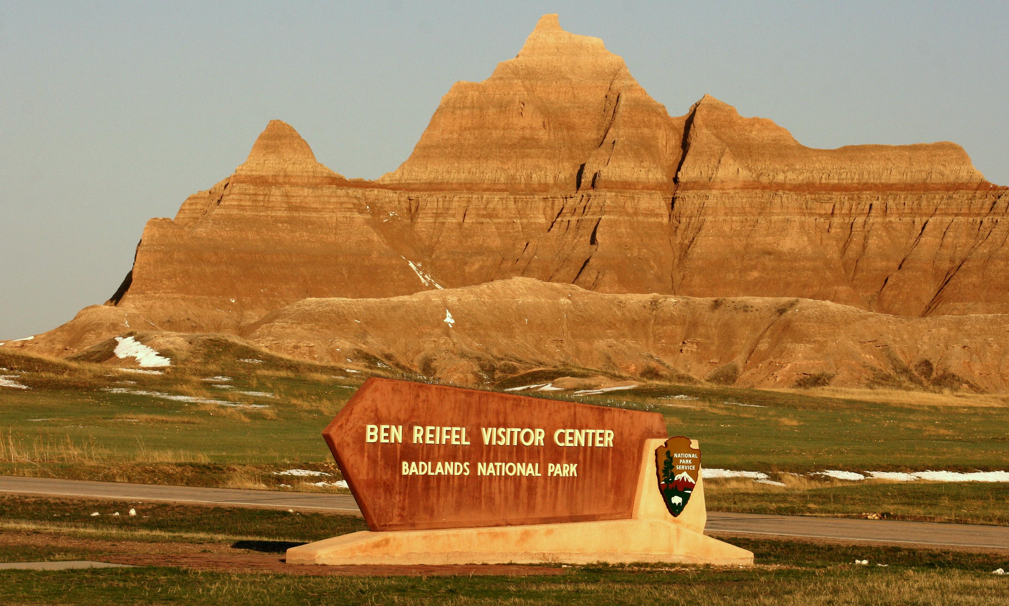 a sign reading ben reifel visitor center sits in front of jagged badlands formations.