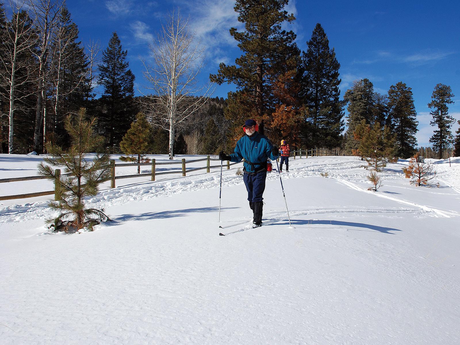 Man cross-country skis on a snowy mesa.