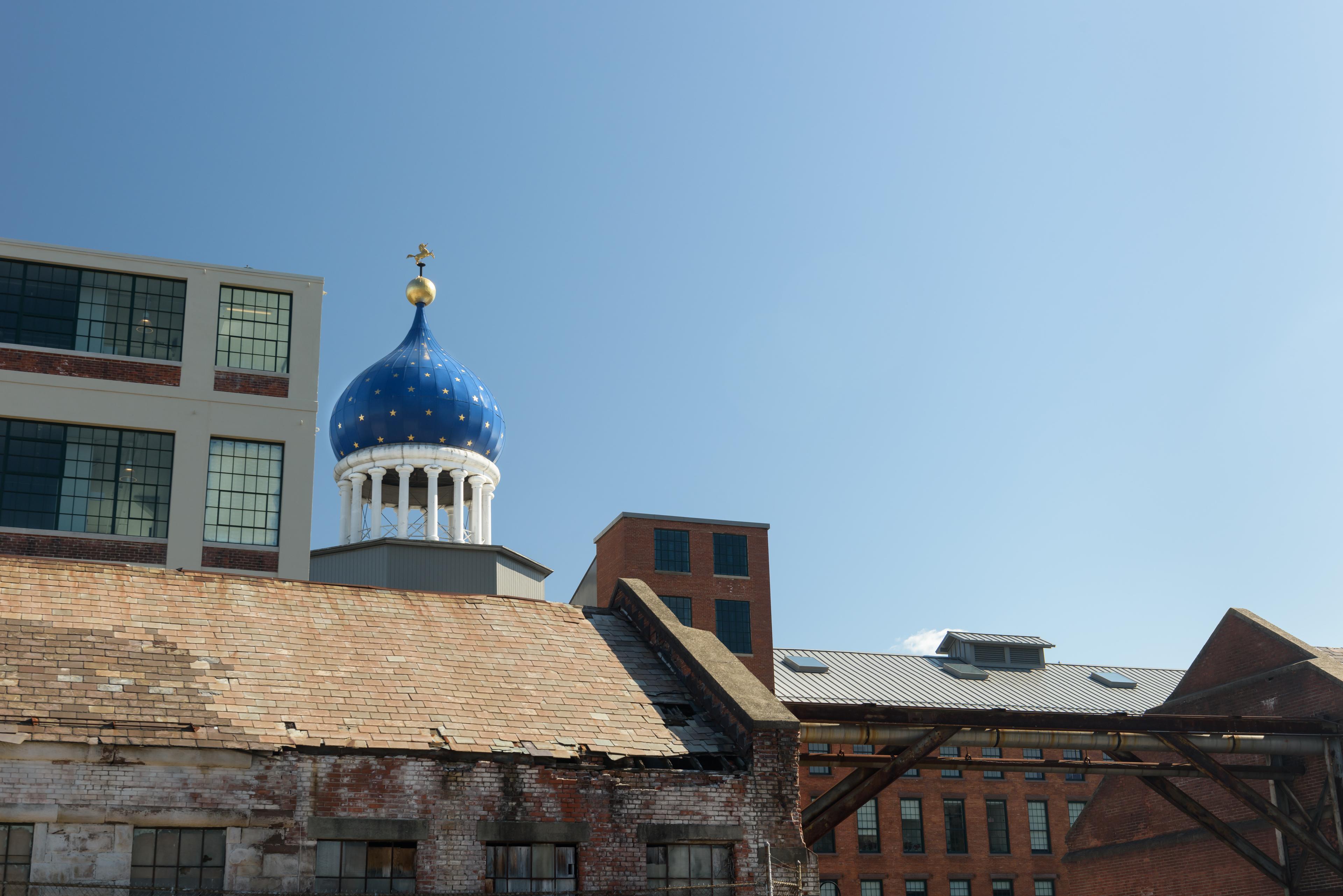 A blue onion dome behind a brownstone building and next to a white building on a clear day.