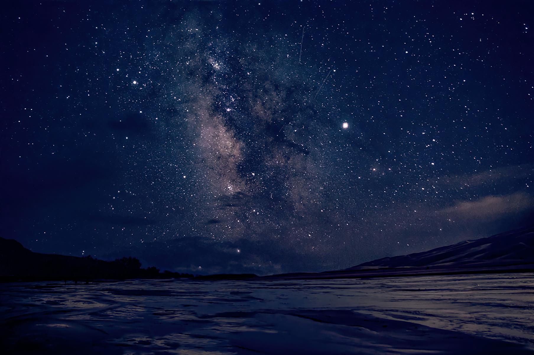 The Milky Way over a shallow stream flowing across sand at night