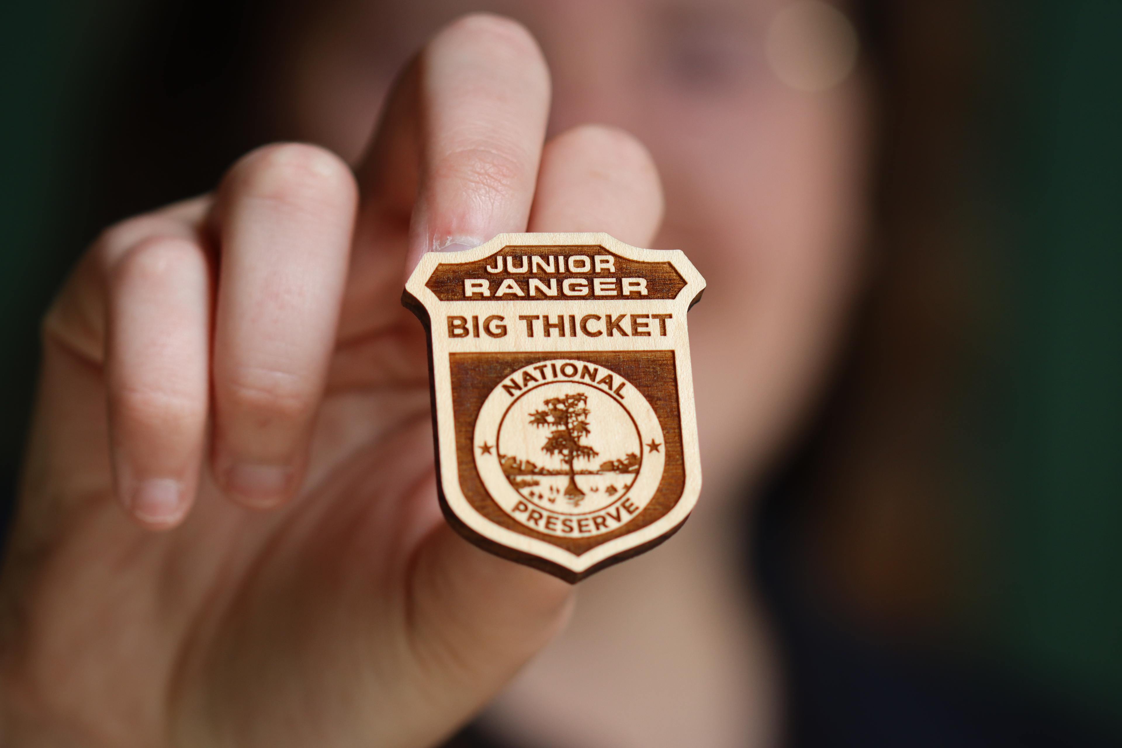 Hand holding a wooden badge that says Junior Ranger, Big Thicket National Preserve.