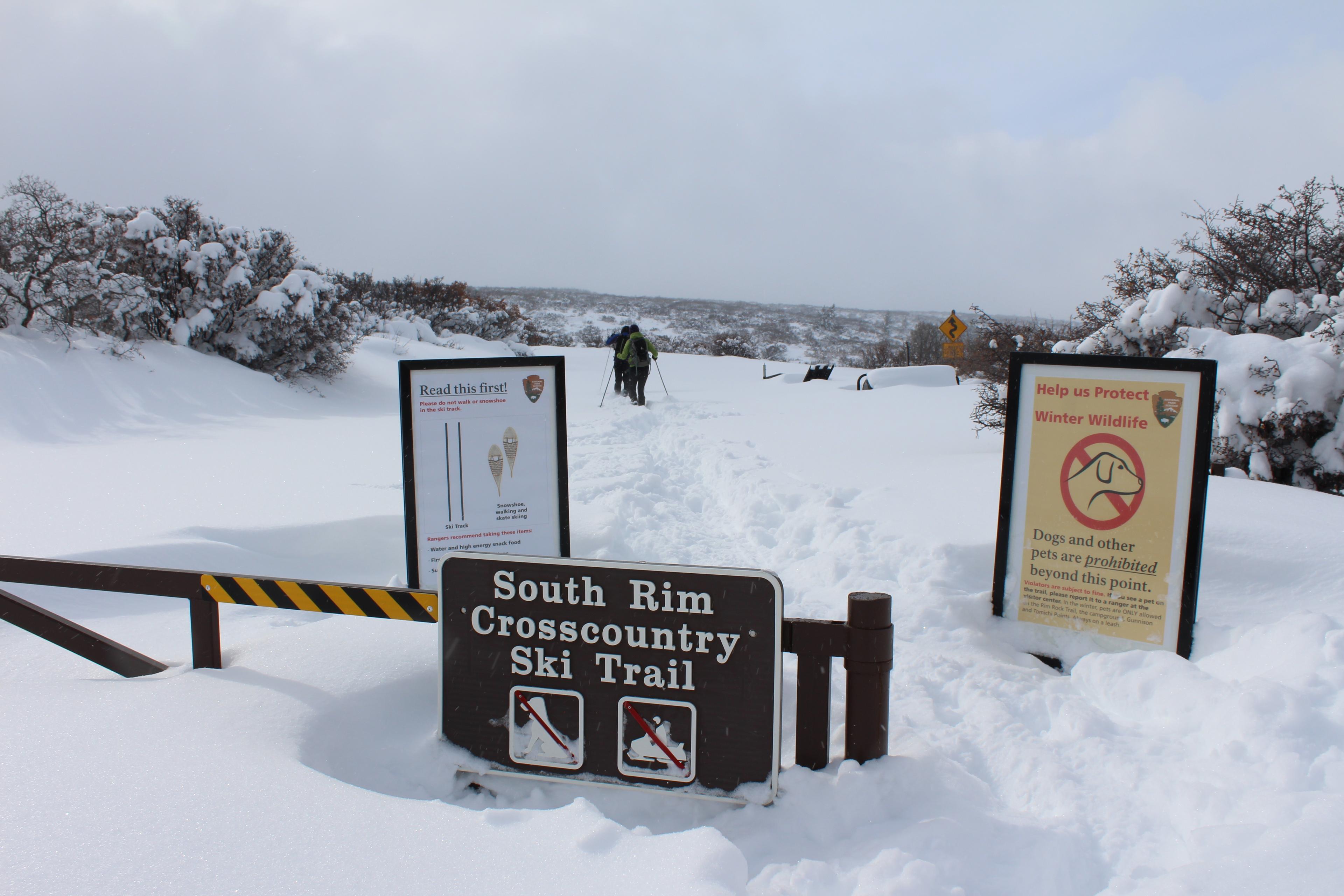 Two large signs behind a gate where people can cross-country ski