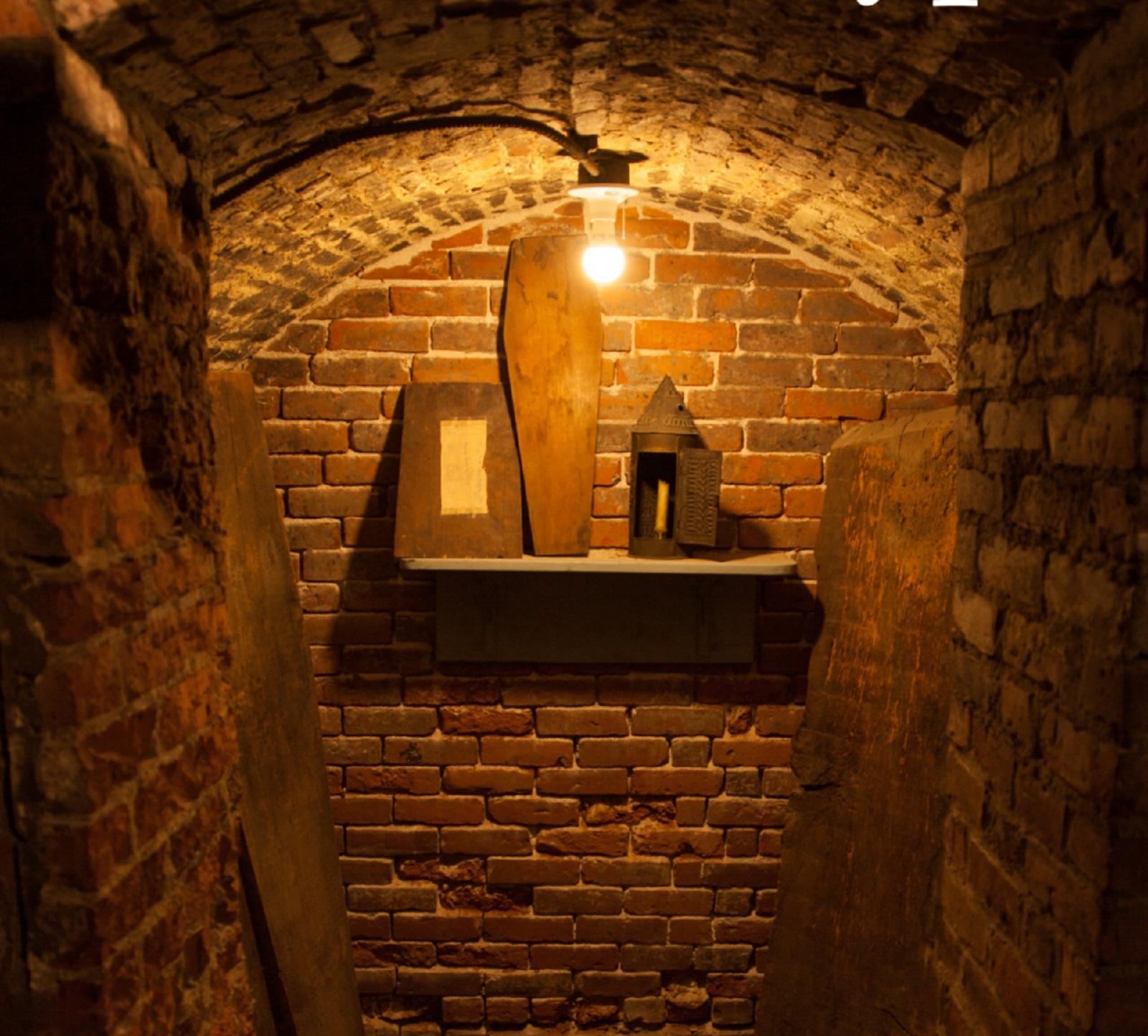 Inside a small red-brick crypt with a shelf that has a couple boxes and a coffin shaped box.