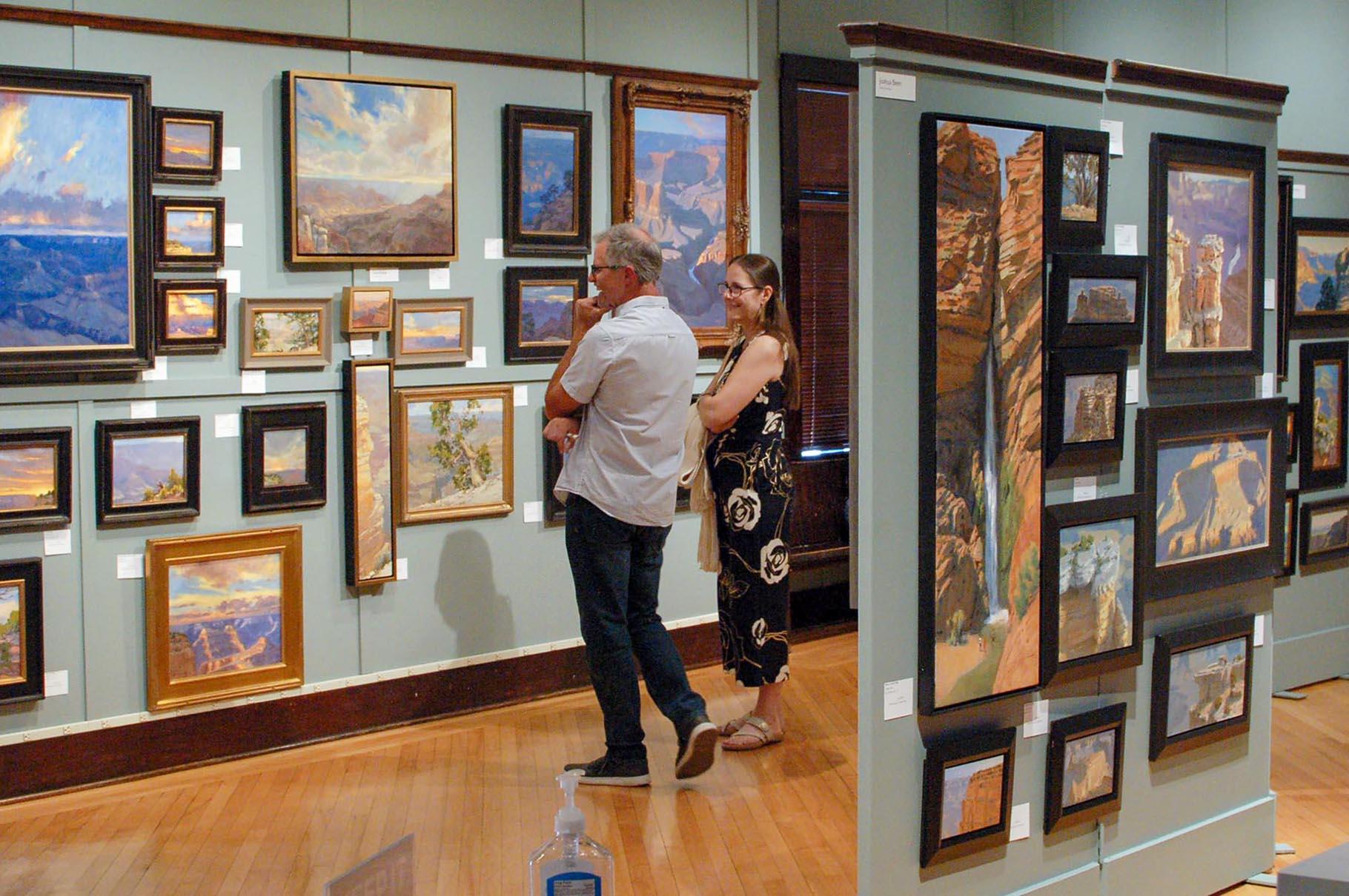 Colorful Grand Canyon paintings of different sizes hanging on walls in an art gallery.