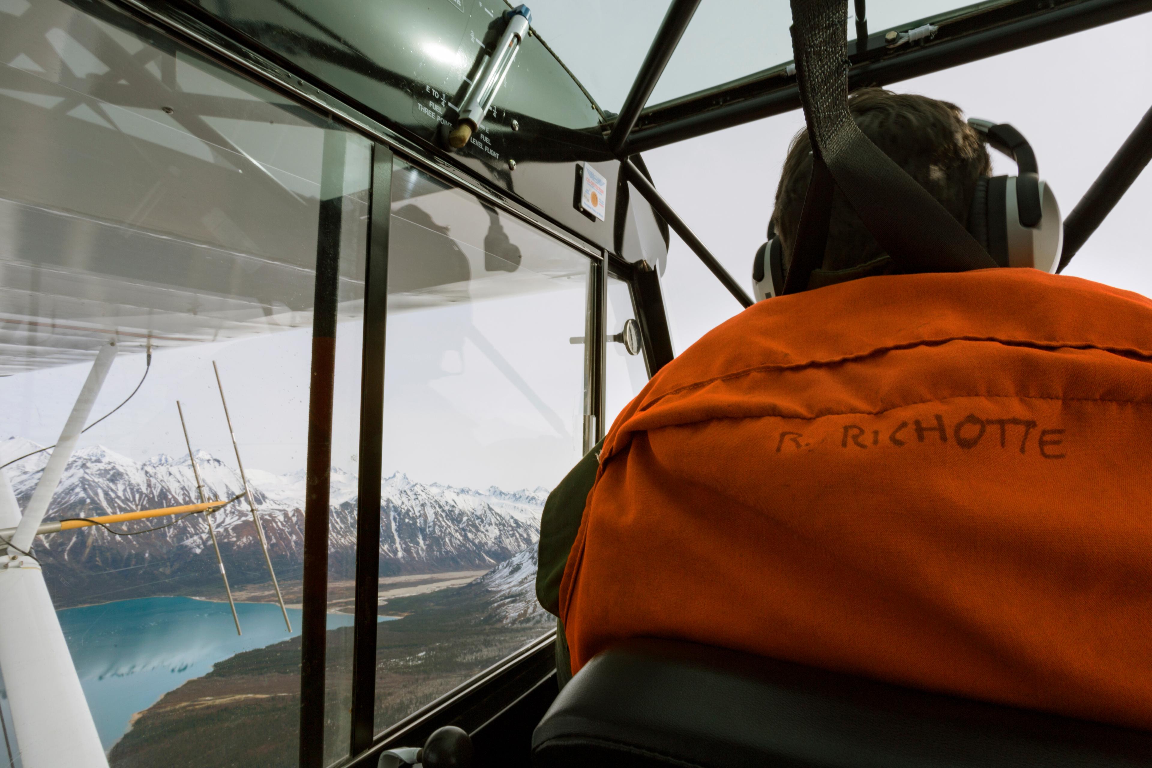 View of pilot inside a plane overlooking a mountain and a lake.