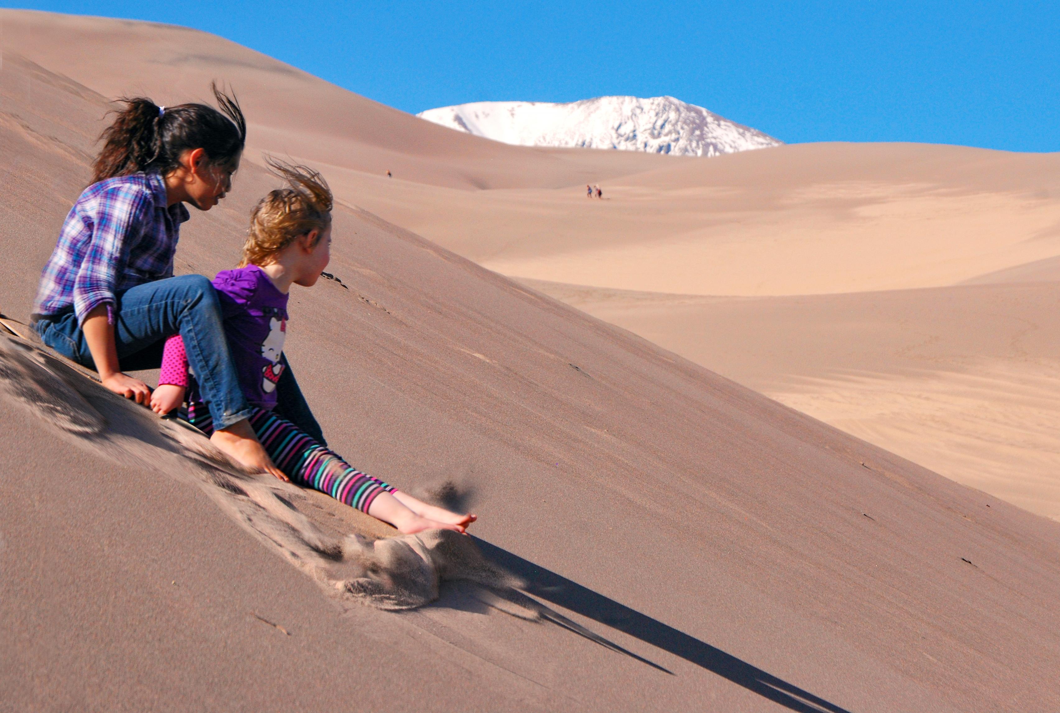 Two girls speed down a dune on a specially designed sand sled.