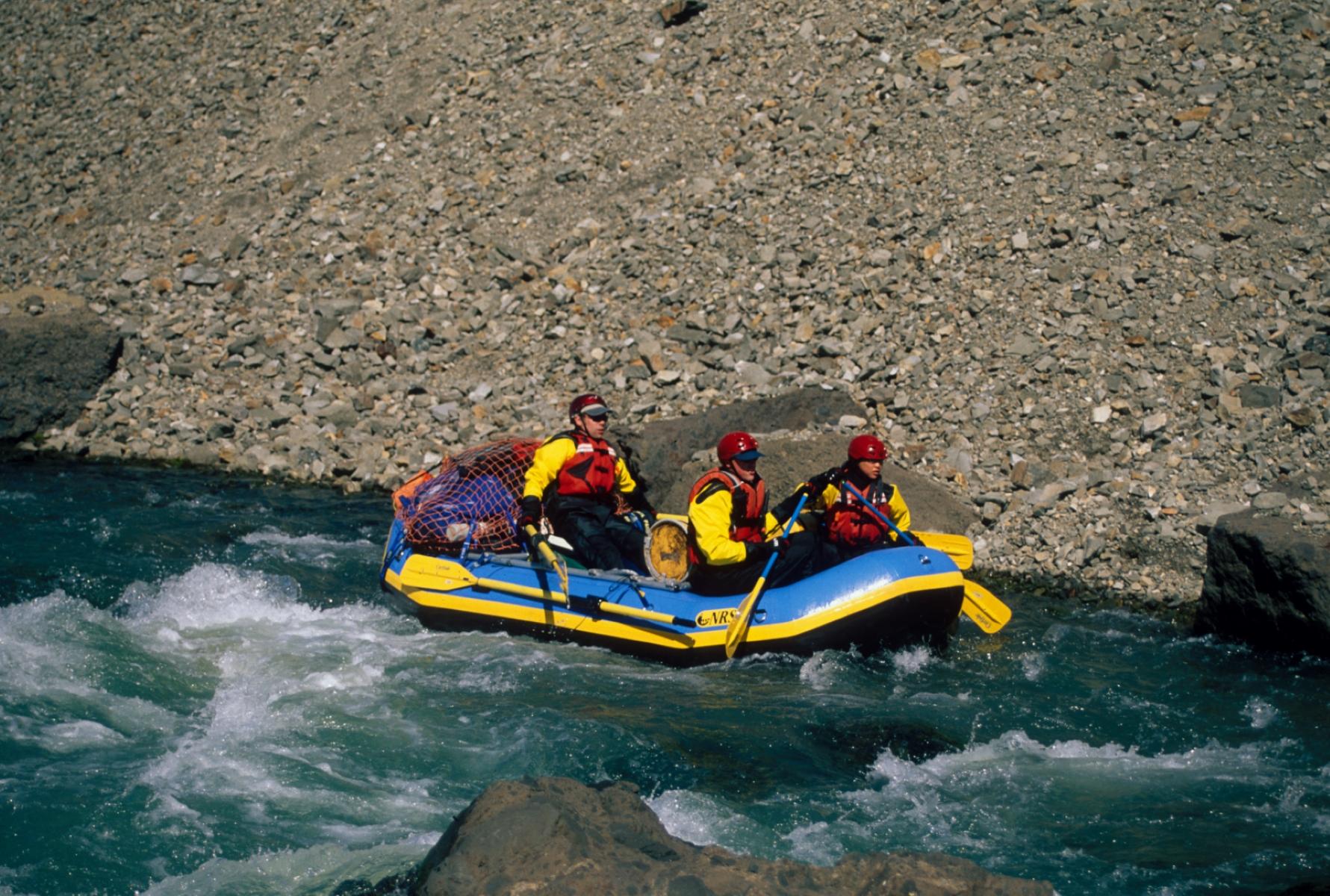 Three people with safety gear in a raft on turquoise and white water