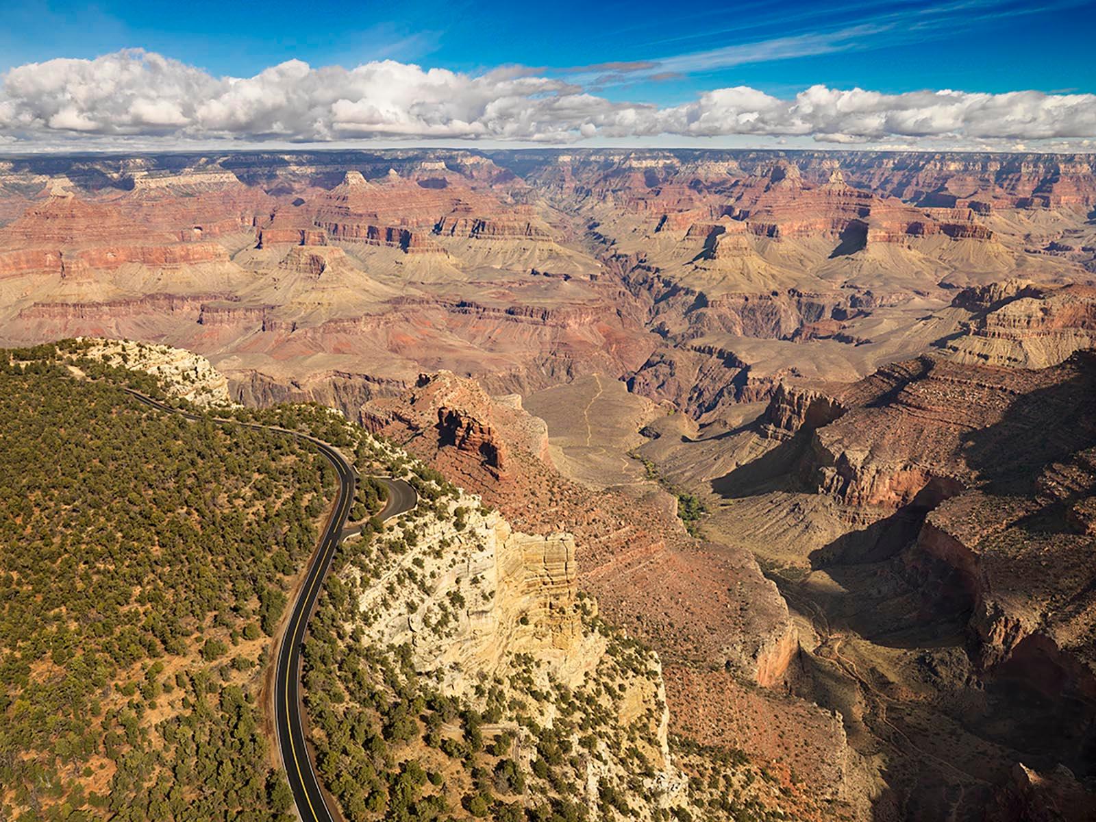 A paved scenic road in a forested area on the edge of a mile deep canyon filled with colorful peaks