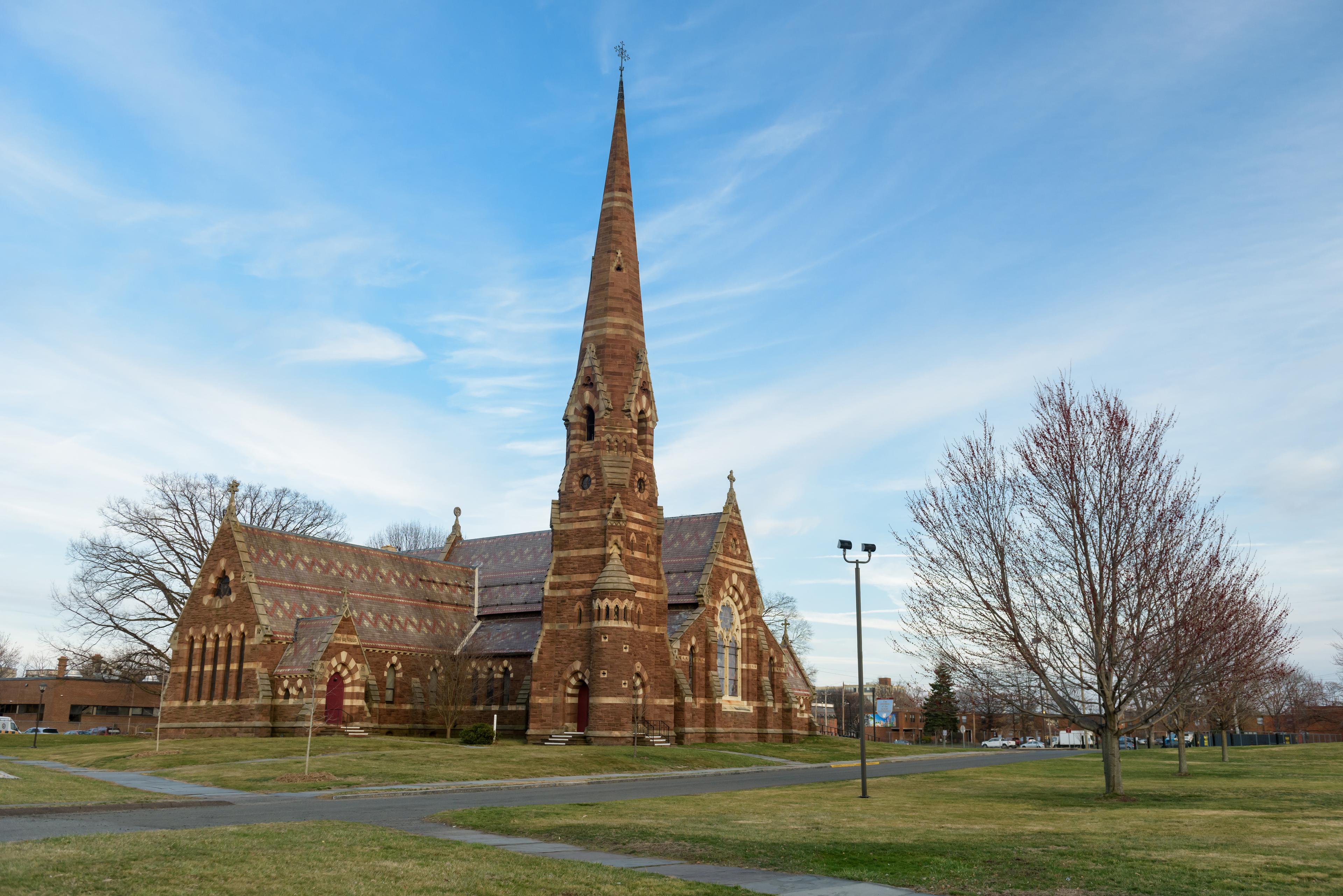 A church with green grass and bare trees in front against a blue sky.