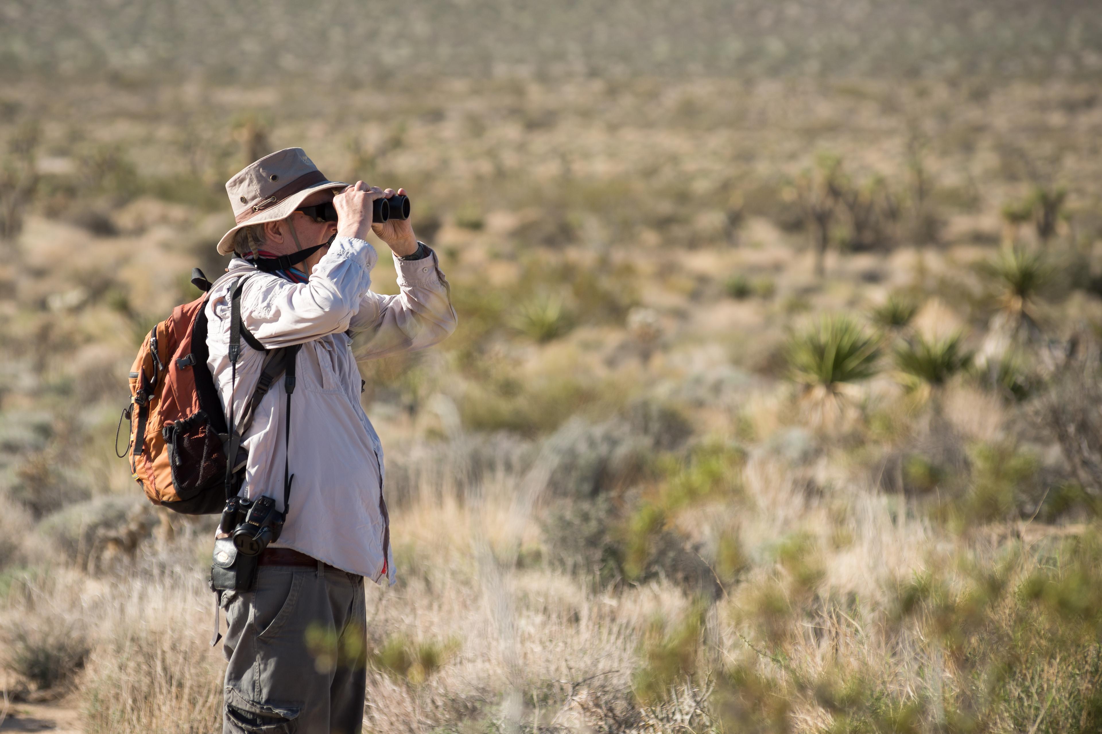 A map holding binoculars up to his face looking into the distance.