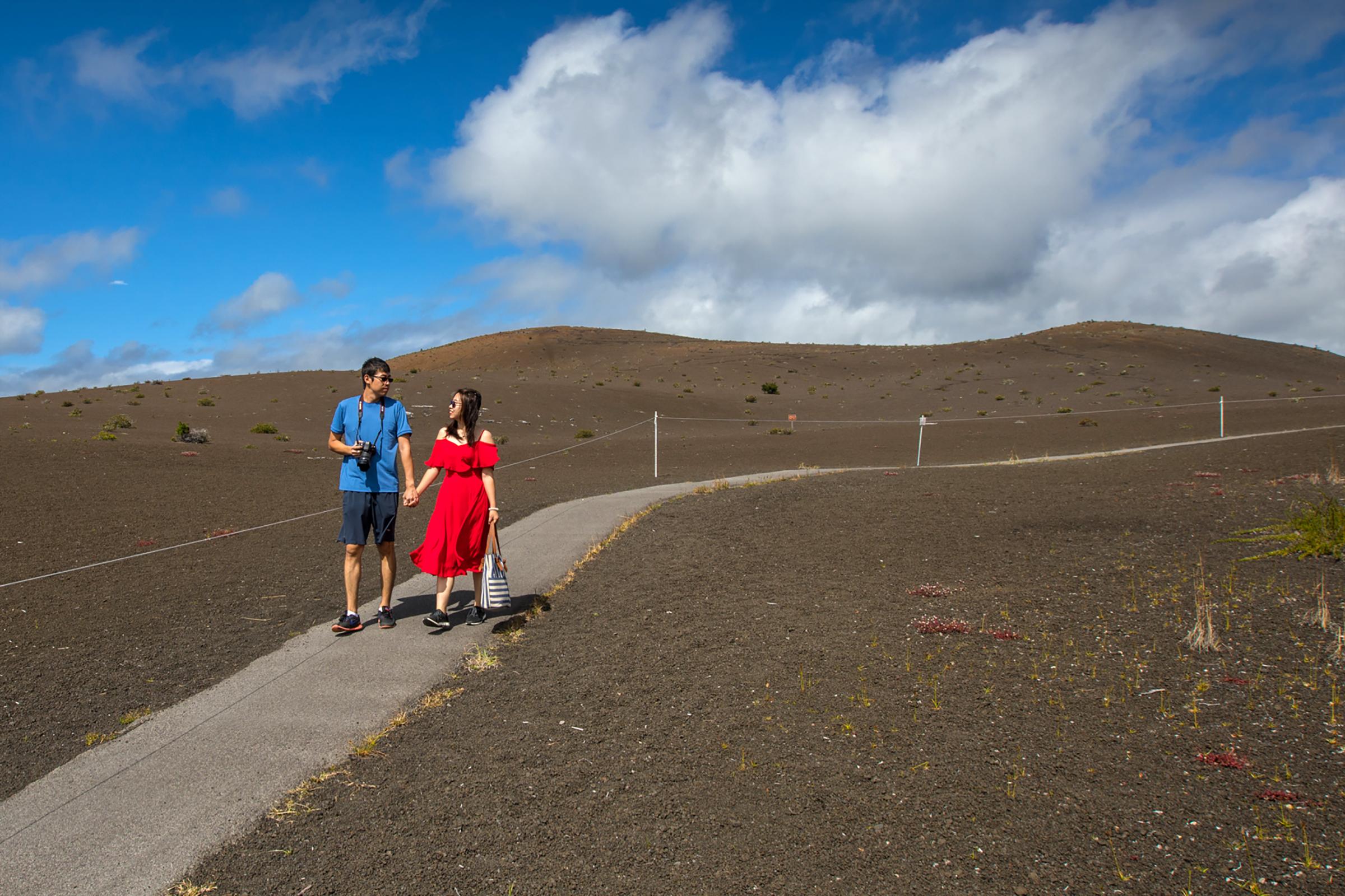 Two people holding hands on a paved path through a cinder-covered landscape