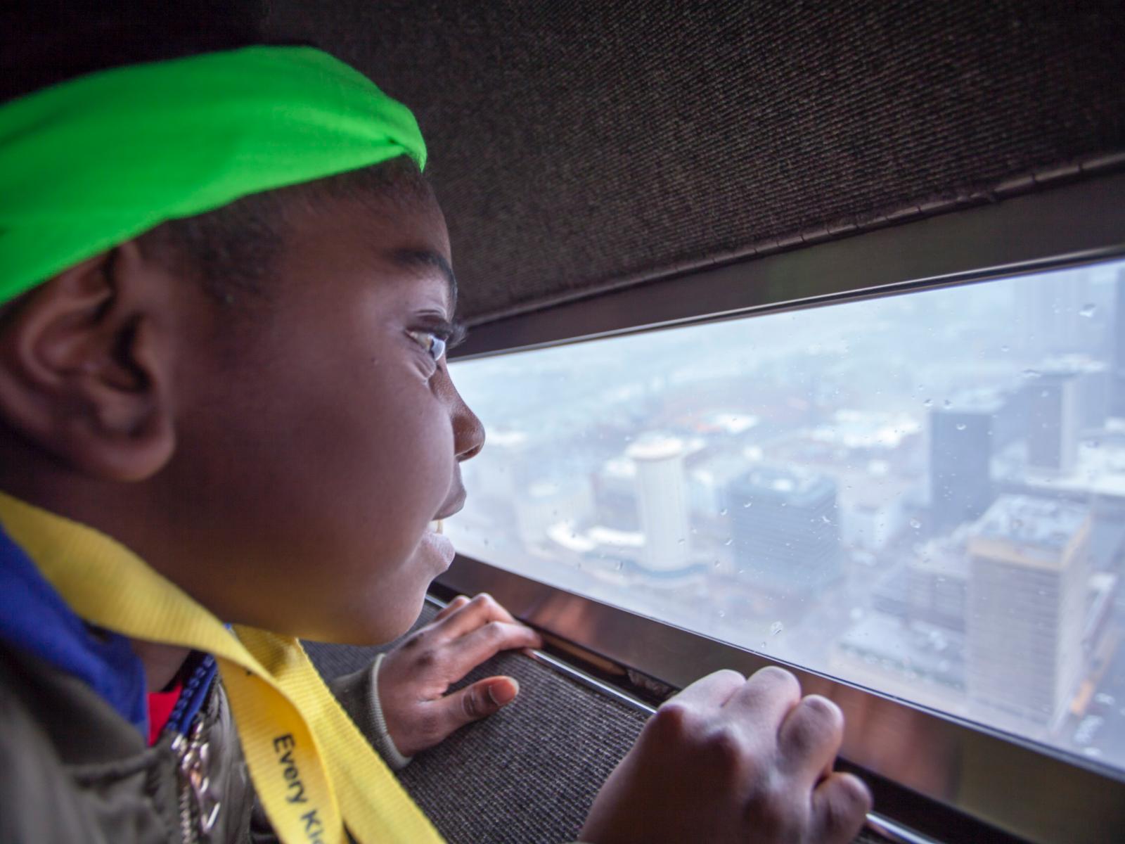 a young African-American girl looks out of the window of the Arch onto the city below