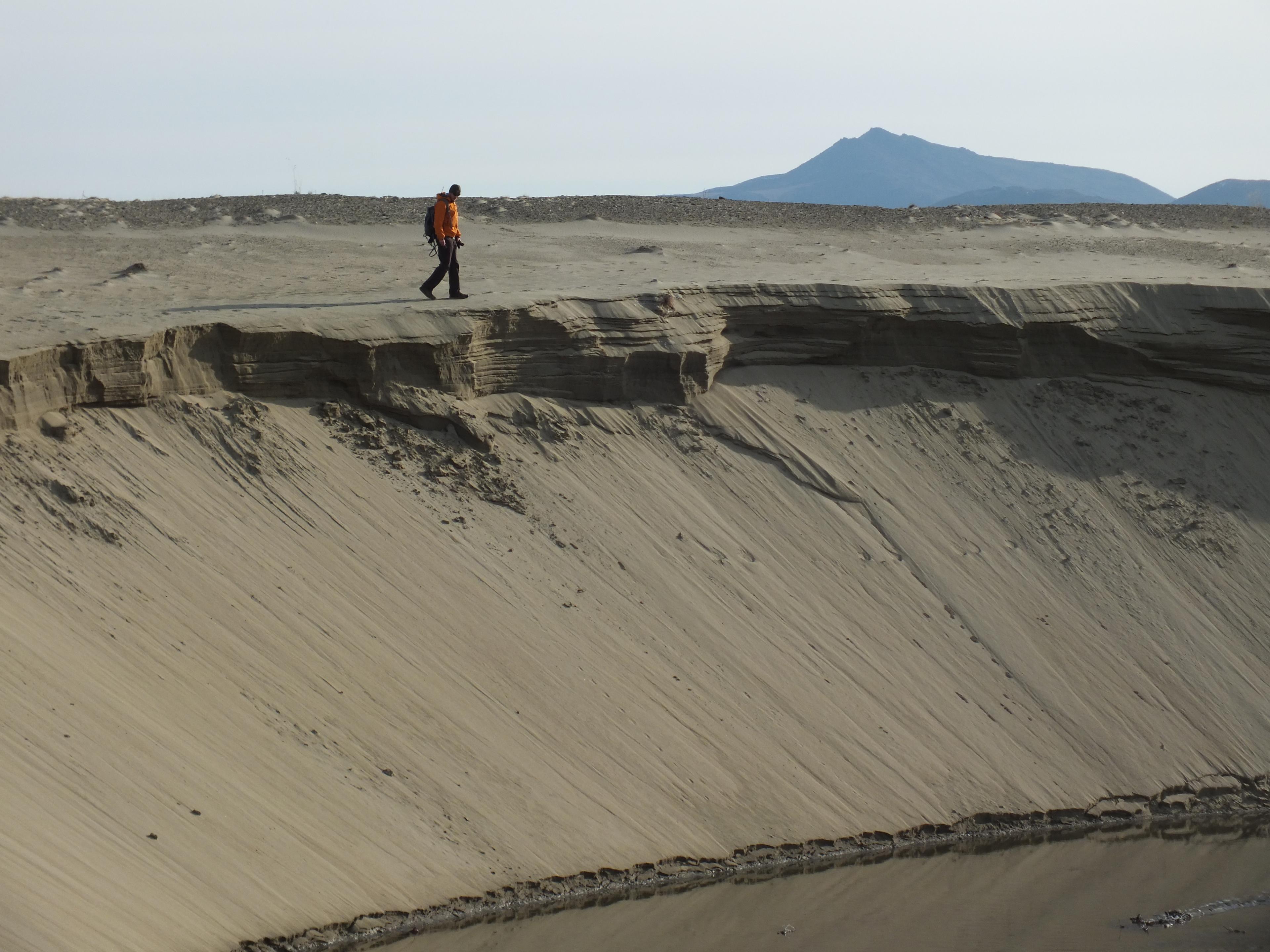 Hiker walking along the edge of a sand dune.