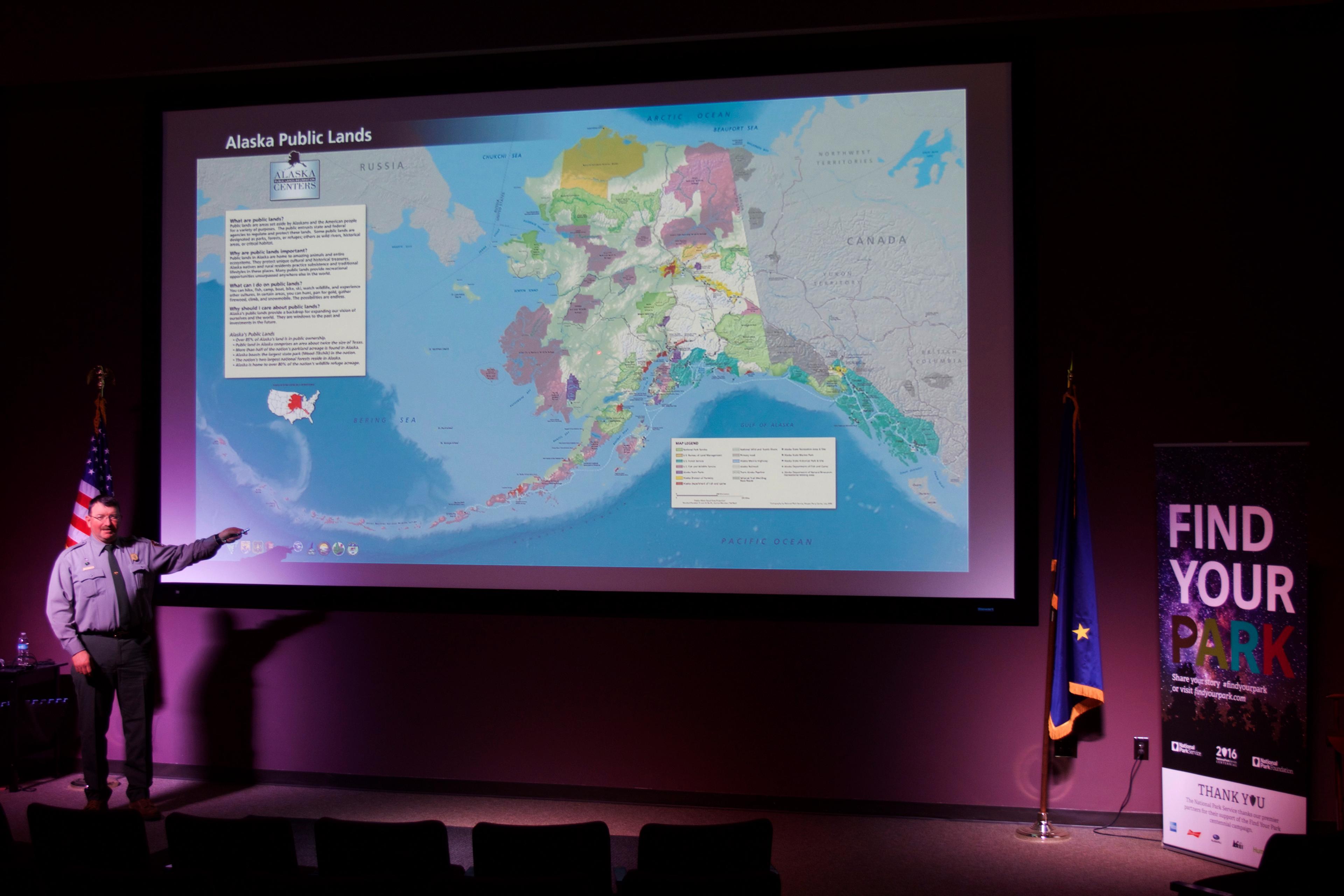 A ranger points to a large map of Alaska on a projector screen