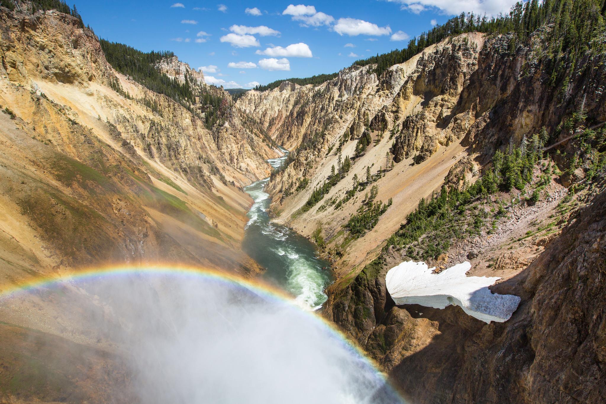 A rainbow is cast in the mist from a waterfall over a river that cuts through a deep canyon.