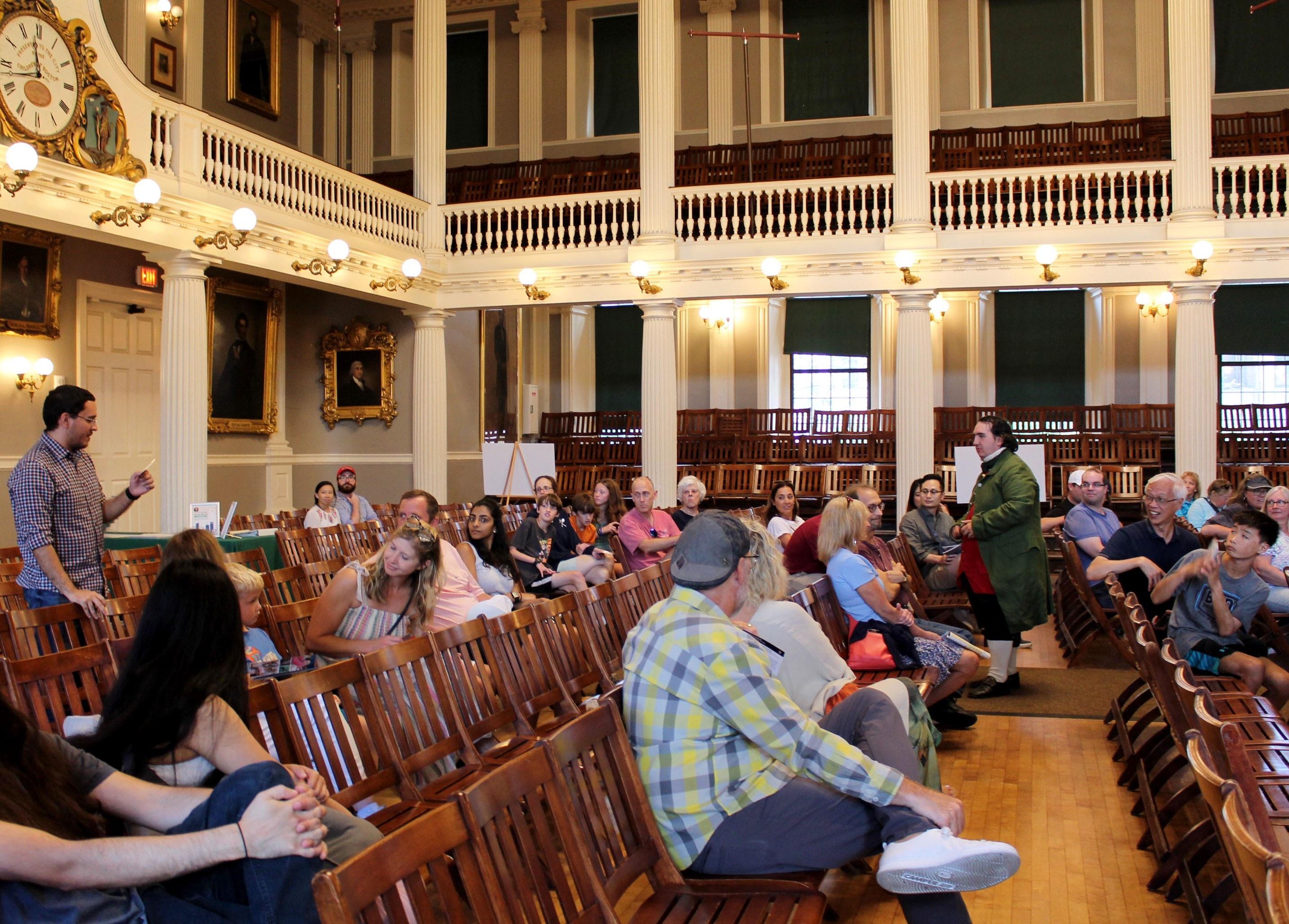 People sitting in chairs in a great hall with a Ranger dressed in period clothing.