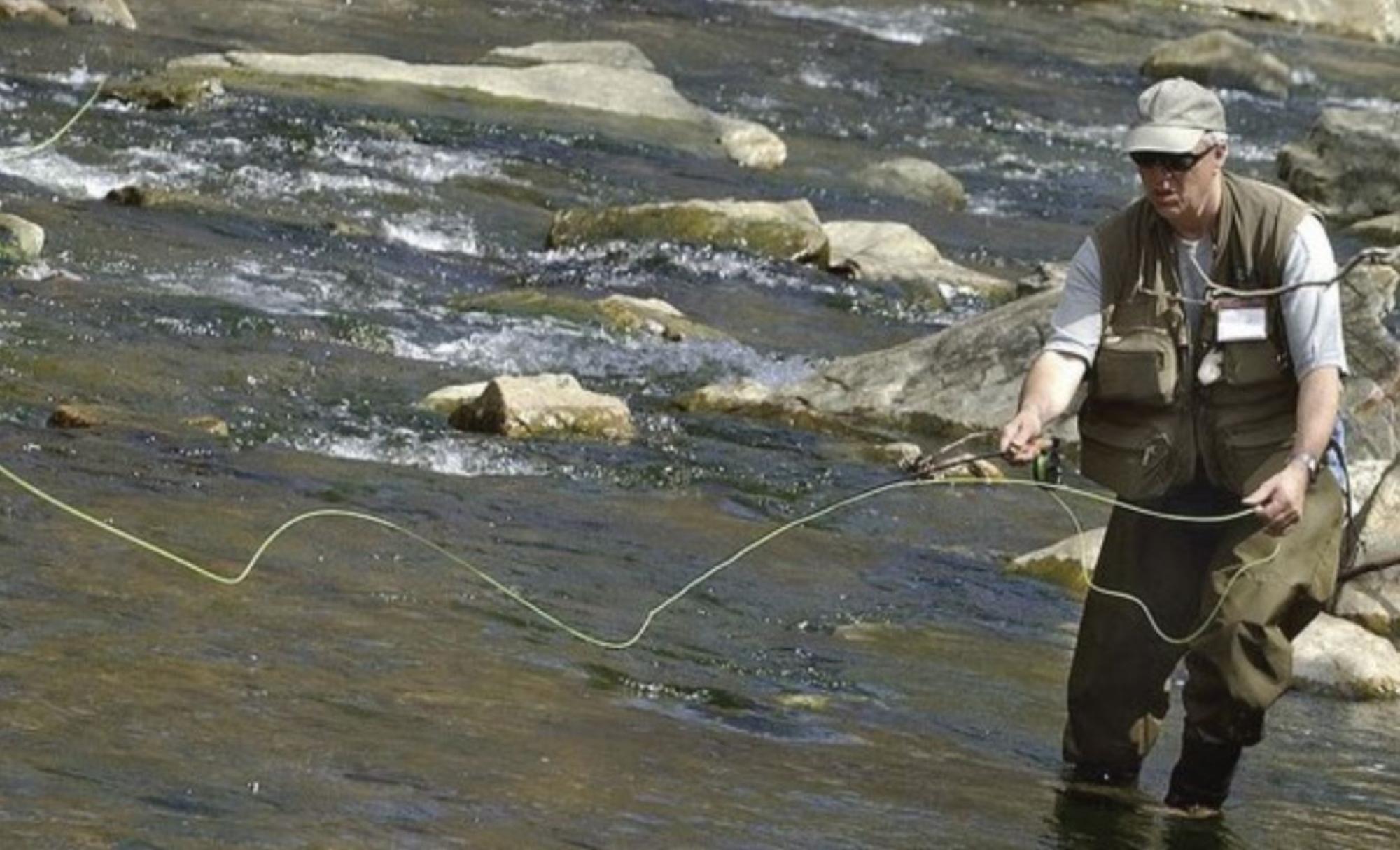 A man in waders and fishing gear standing in a creek.