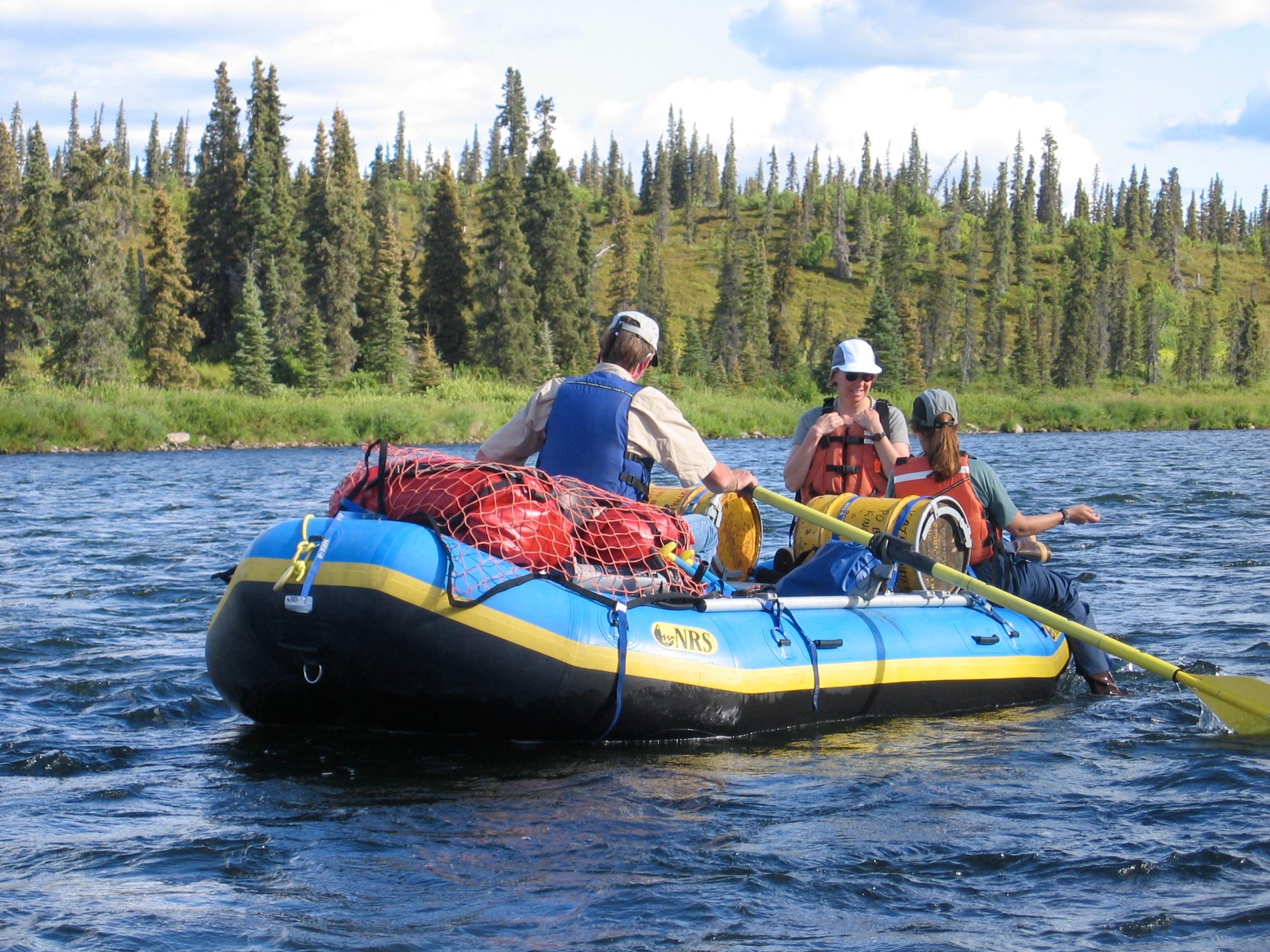 Three people in a raft on the water with trees in the background