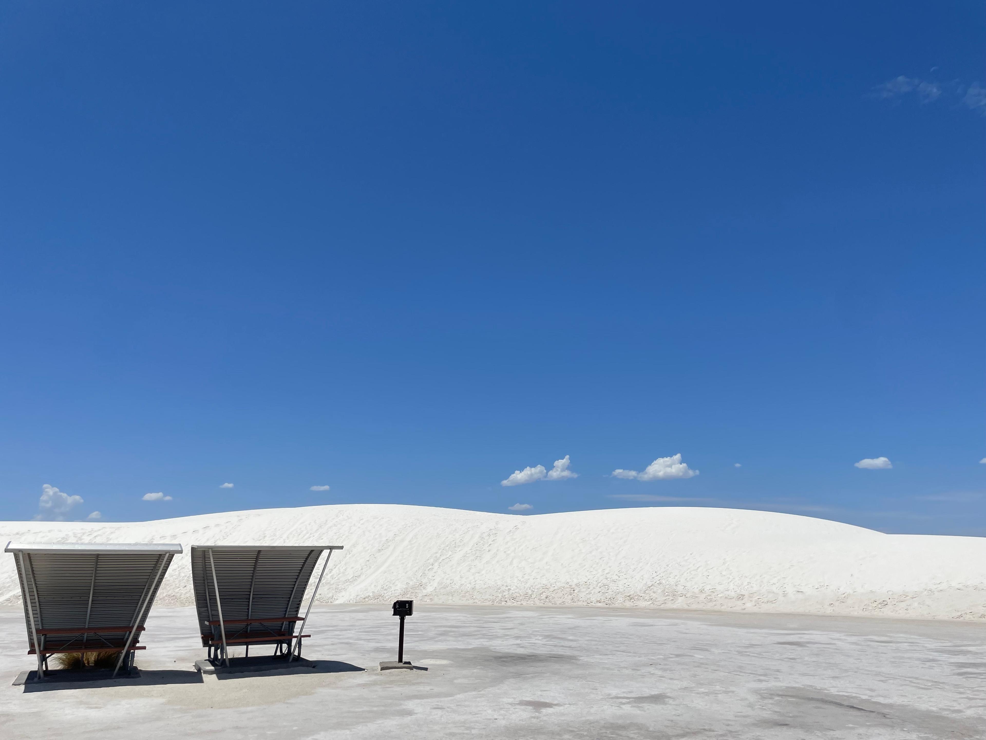 two picnic shelters with metal toppers sit in front of a tall white dune