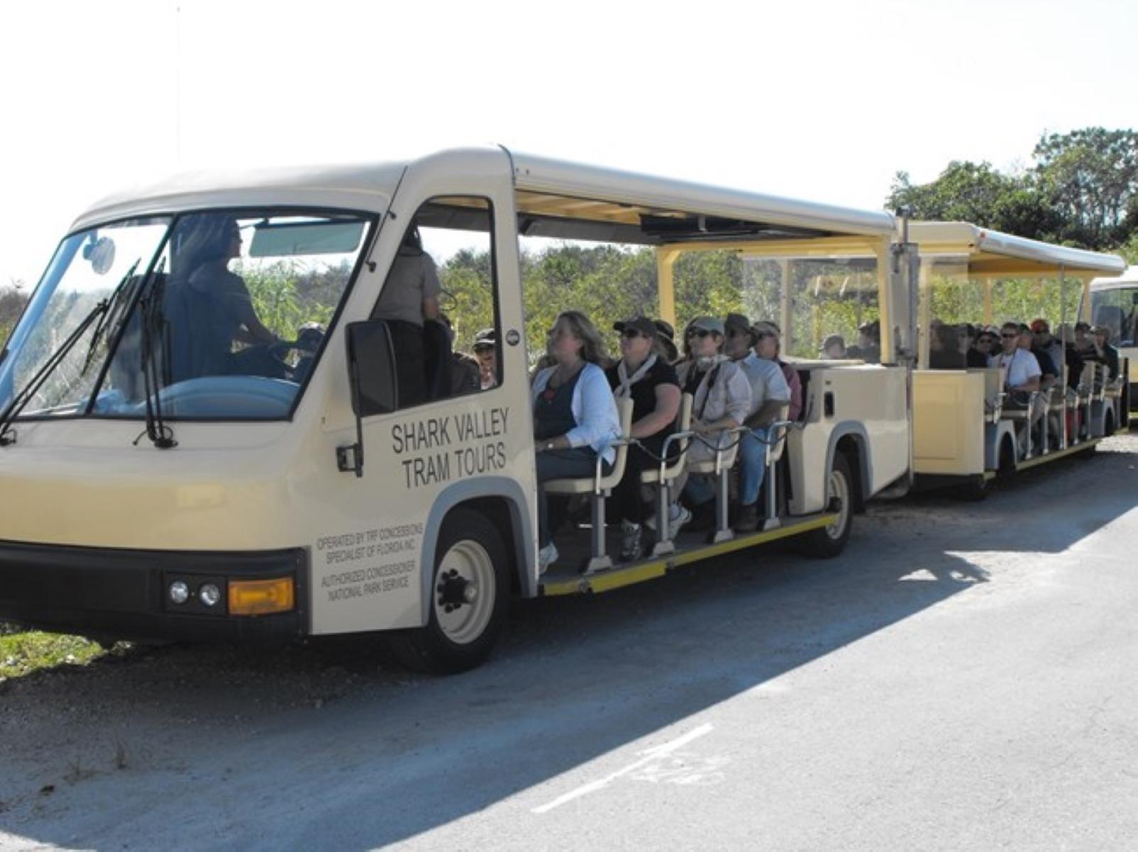 Passengers sit in a beige open air tram. A ranger sits facing the audience.