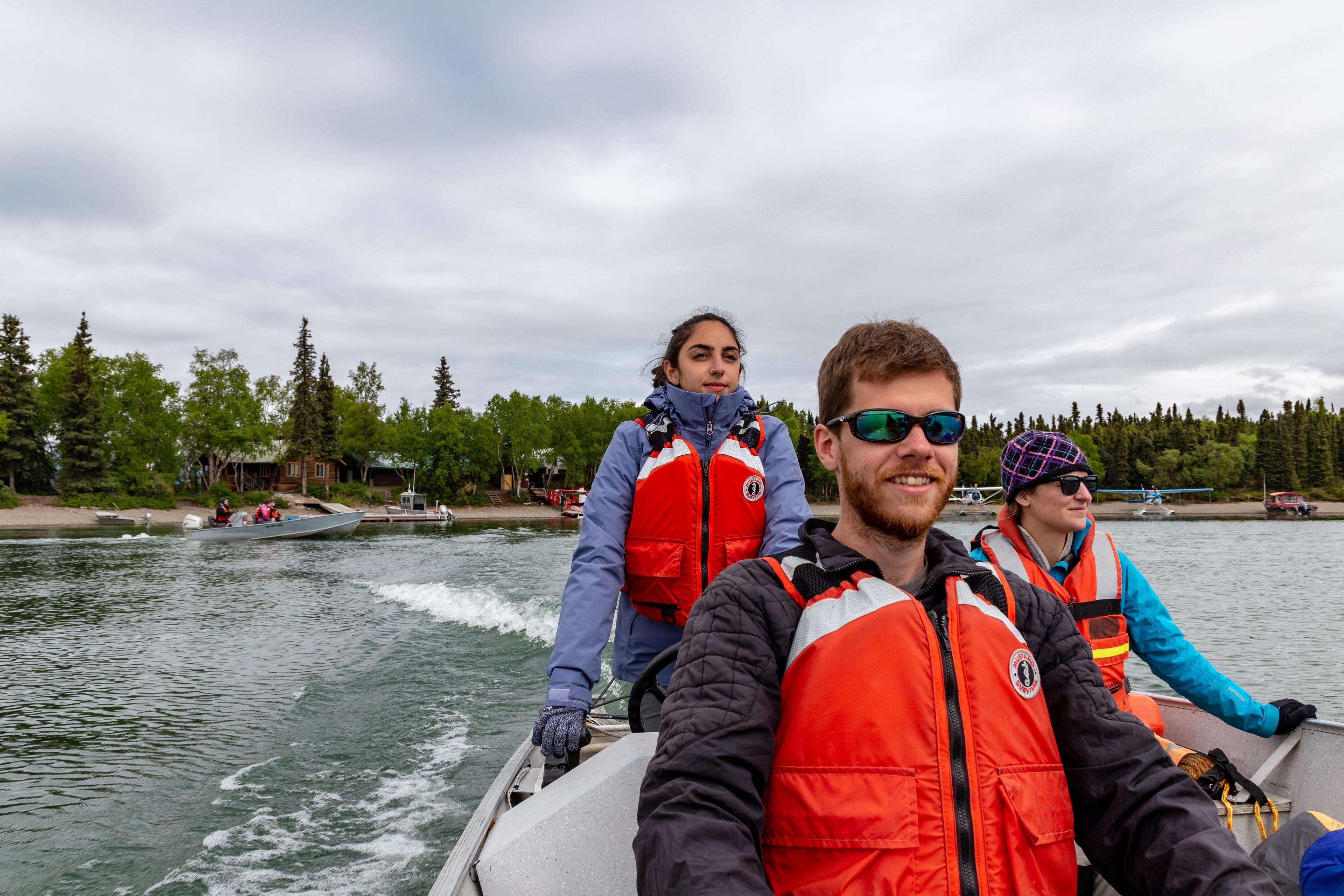 3 people wearing PFDs ride in a boat from the shore of Port Alsworth