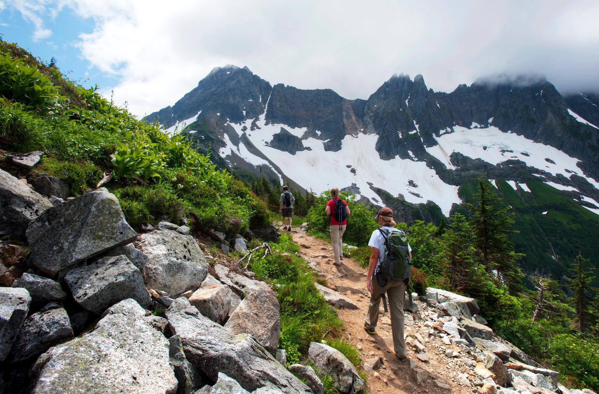 Two hikers walk along a trail with mountains in the distance.