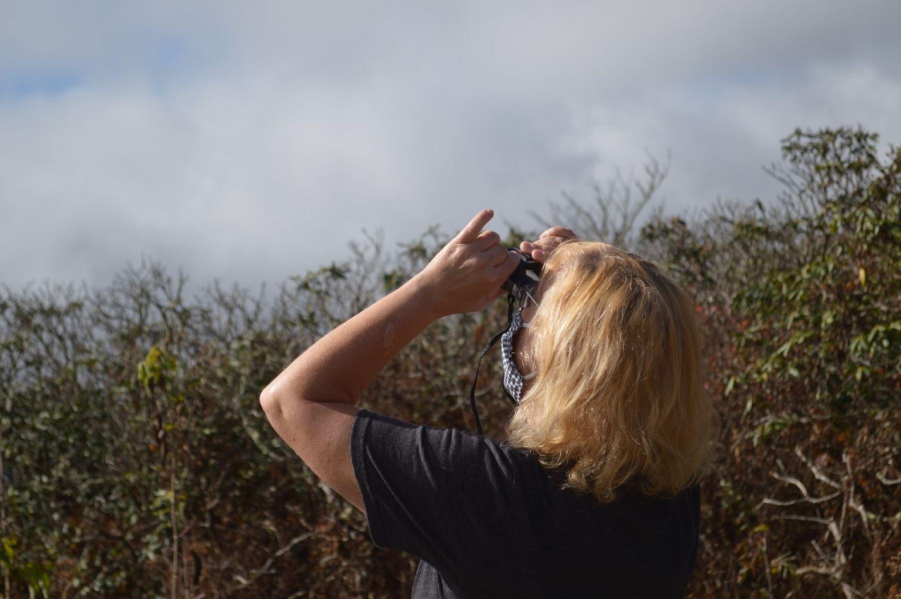 A woman using binoculars looks up in the sky