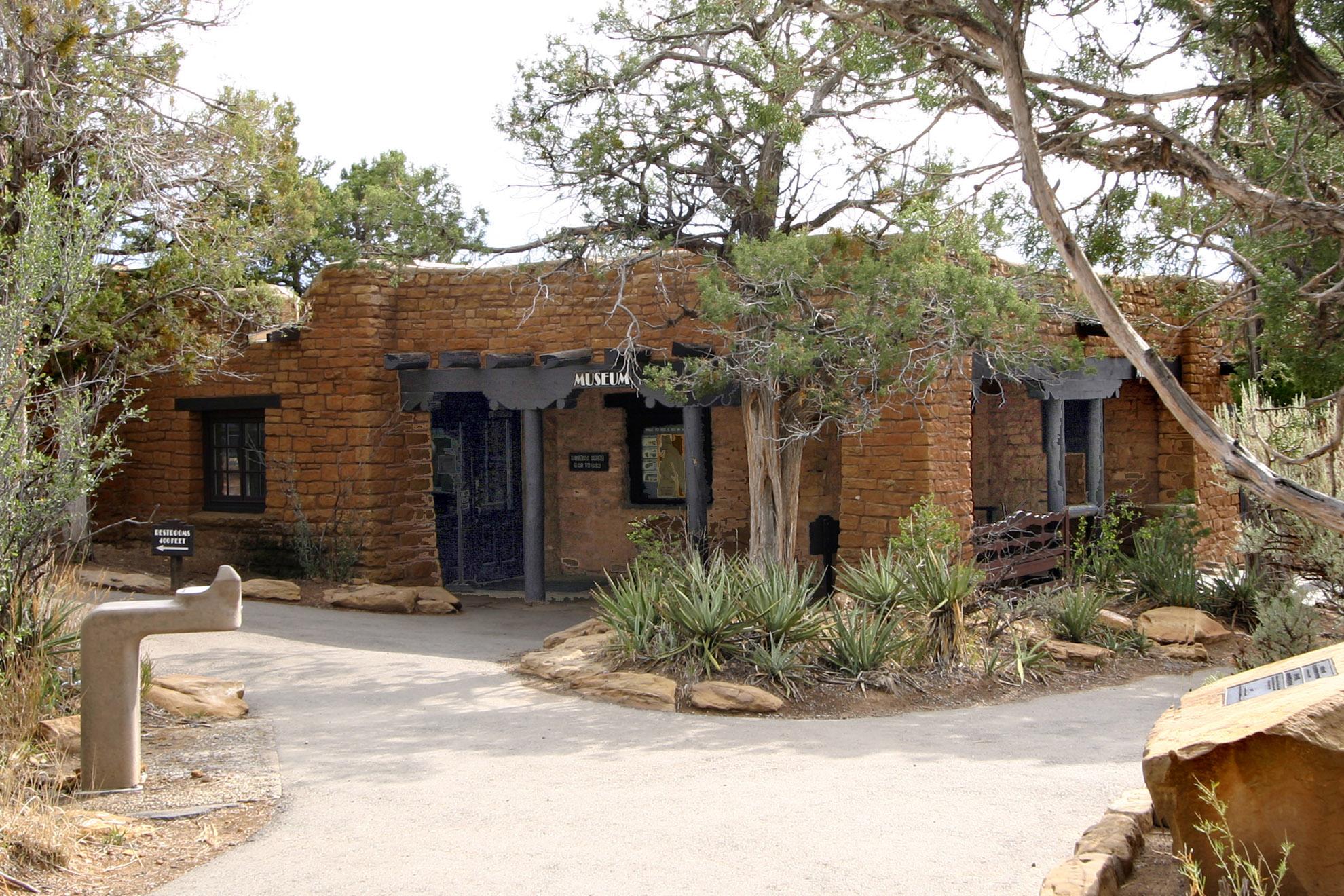 Rock and timber building surrounded by yucca, brush, and trees.