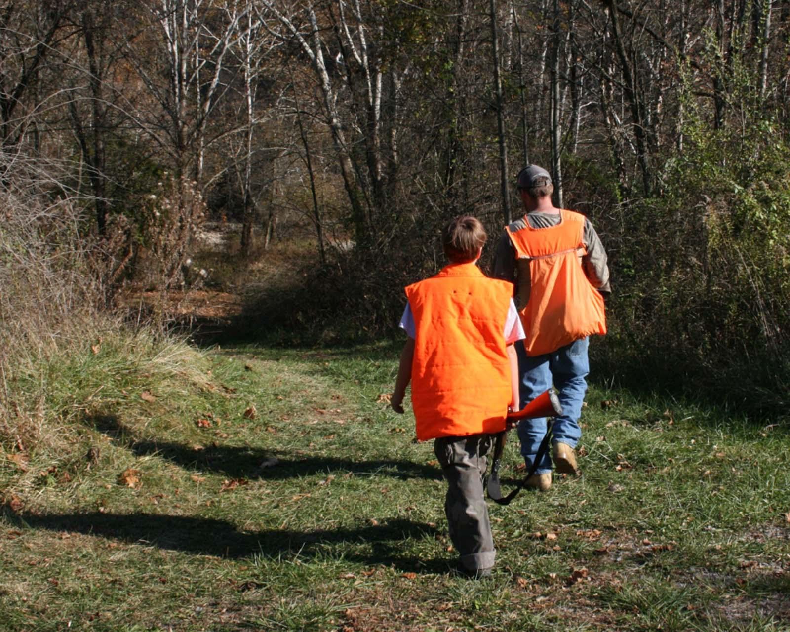 Two men walking in the woods wearing blaze orange hunting vests.