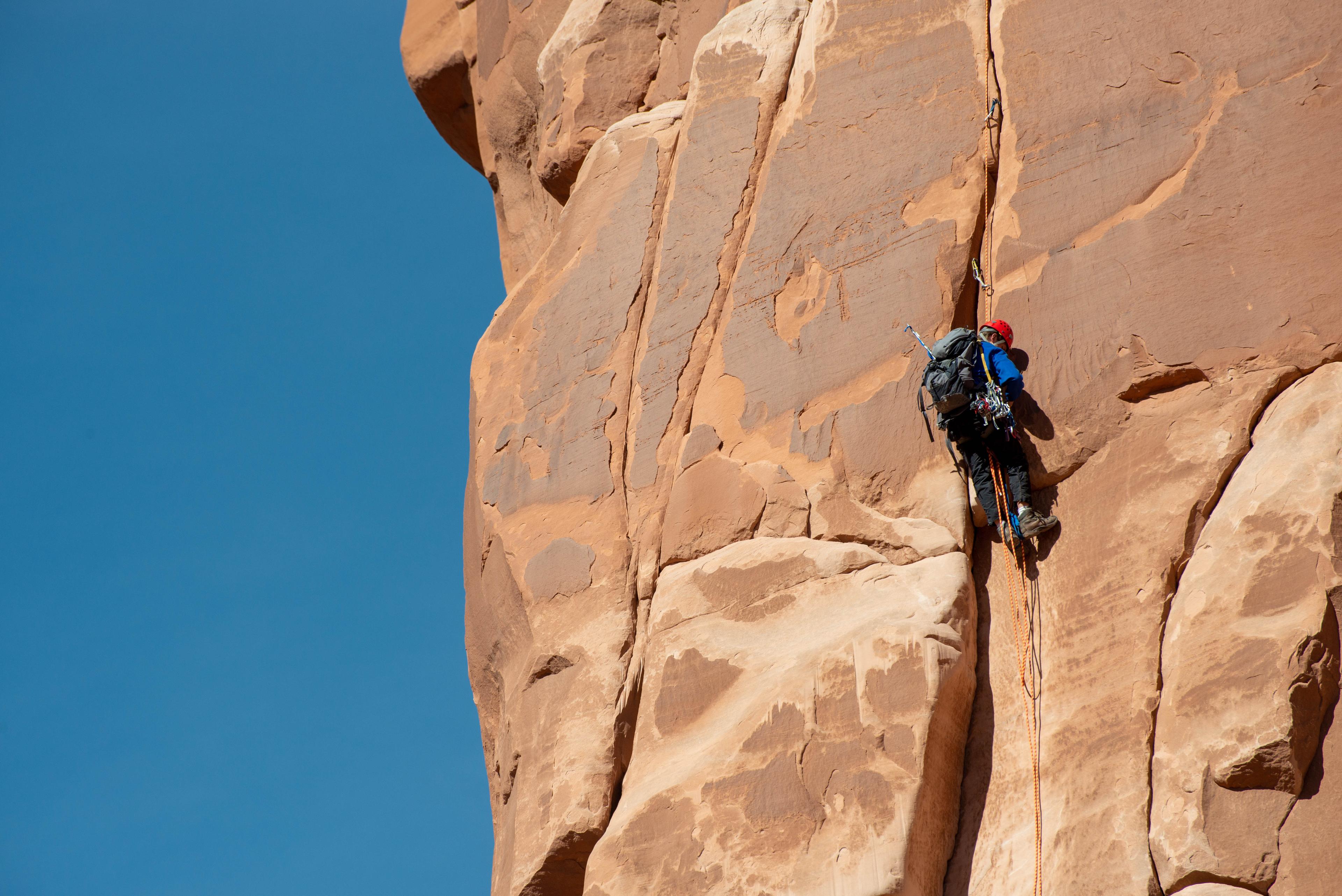 rock climber on vertical tan sandstone face, blue sky in background