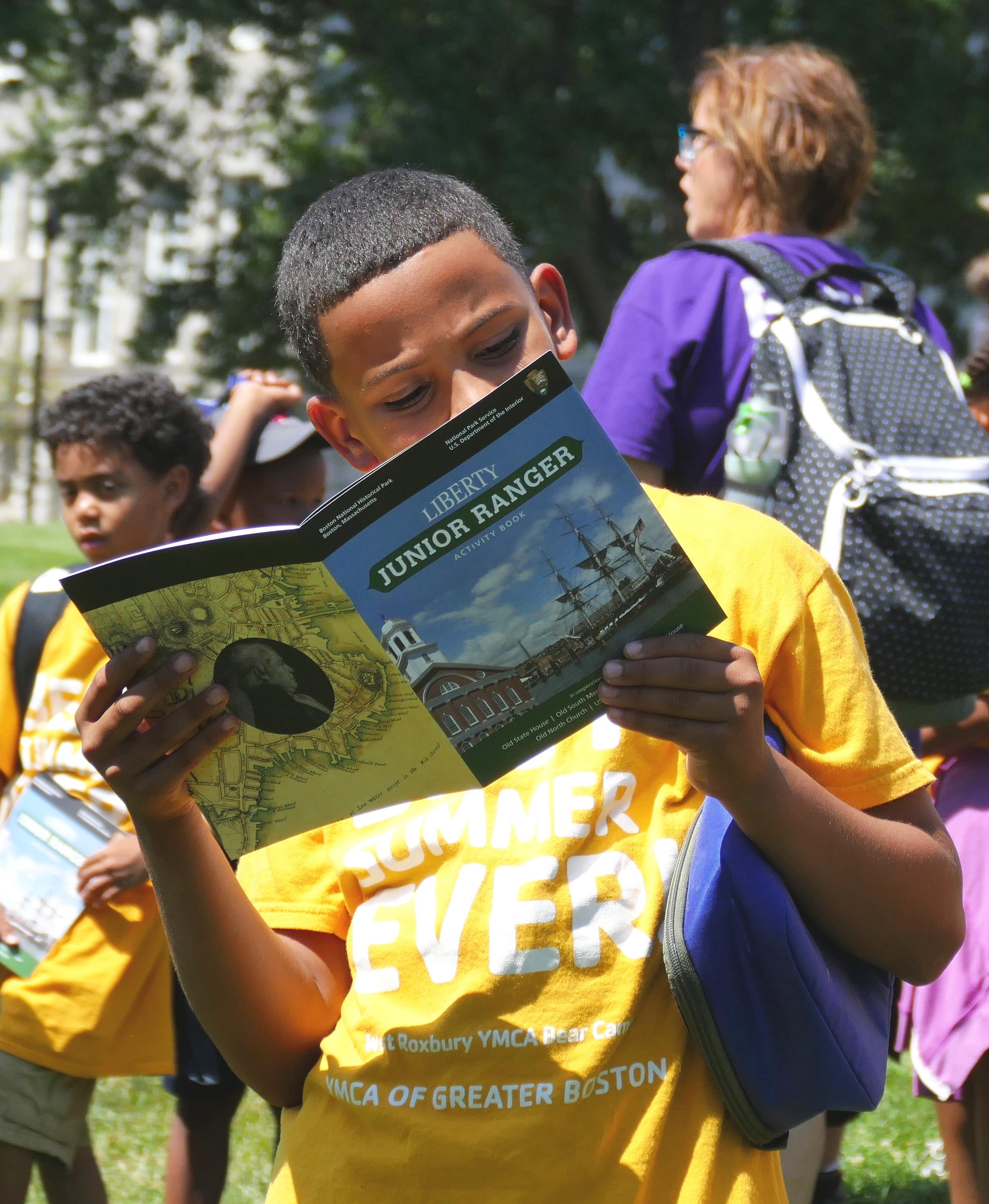 An African American child holding up the "Liberty Junior Ranger Activity Book."