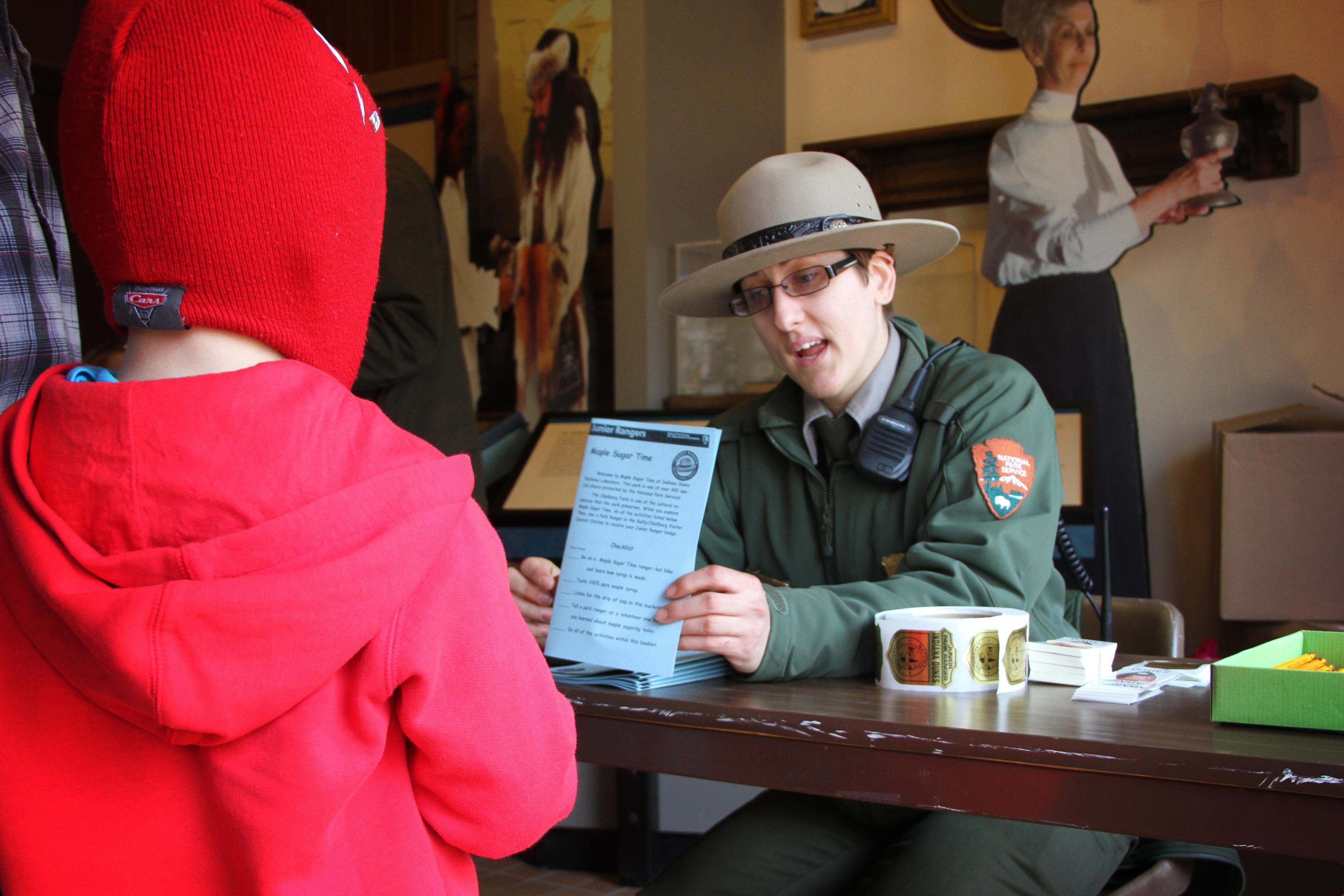 Ranger talks to child while holding a Junior Ranger booklet