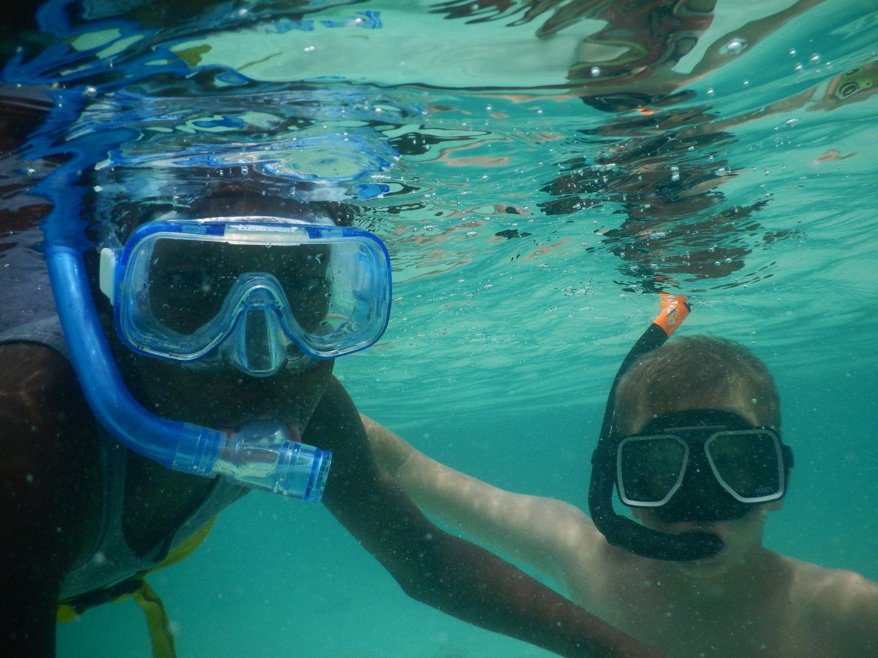 Two young swimmers wear mask and snorkel in clear water.