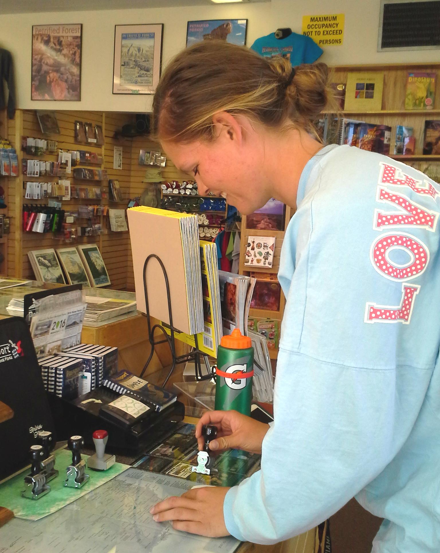 Woman inside stamping in booklet on counter, displays in background.