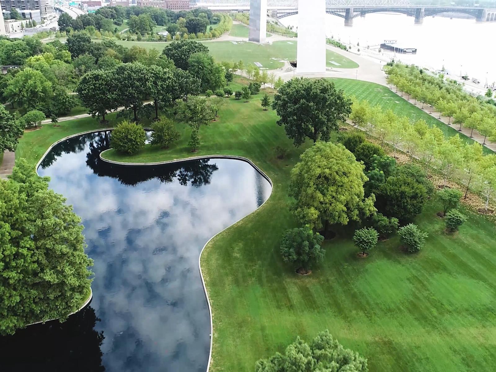 looking down at a pond with a curving edge reflecting clouds surrounded by green landscape