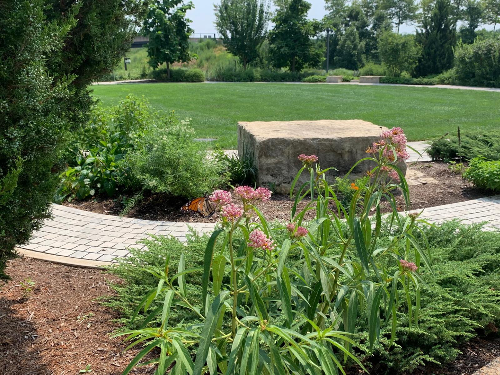 a stone block along a curved path in front of a green lawn with plants surrounding