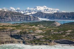 Glaciers loom over the ocean with large snowy mountains rising into blue skies