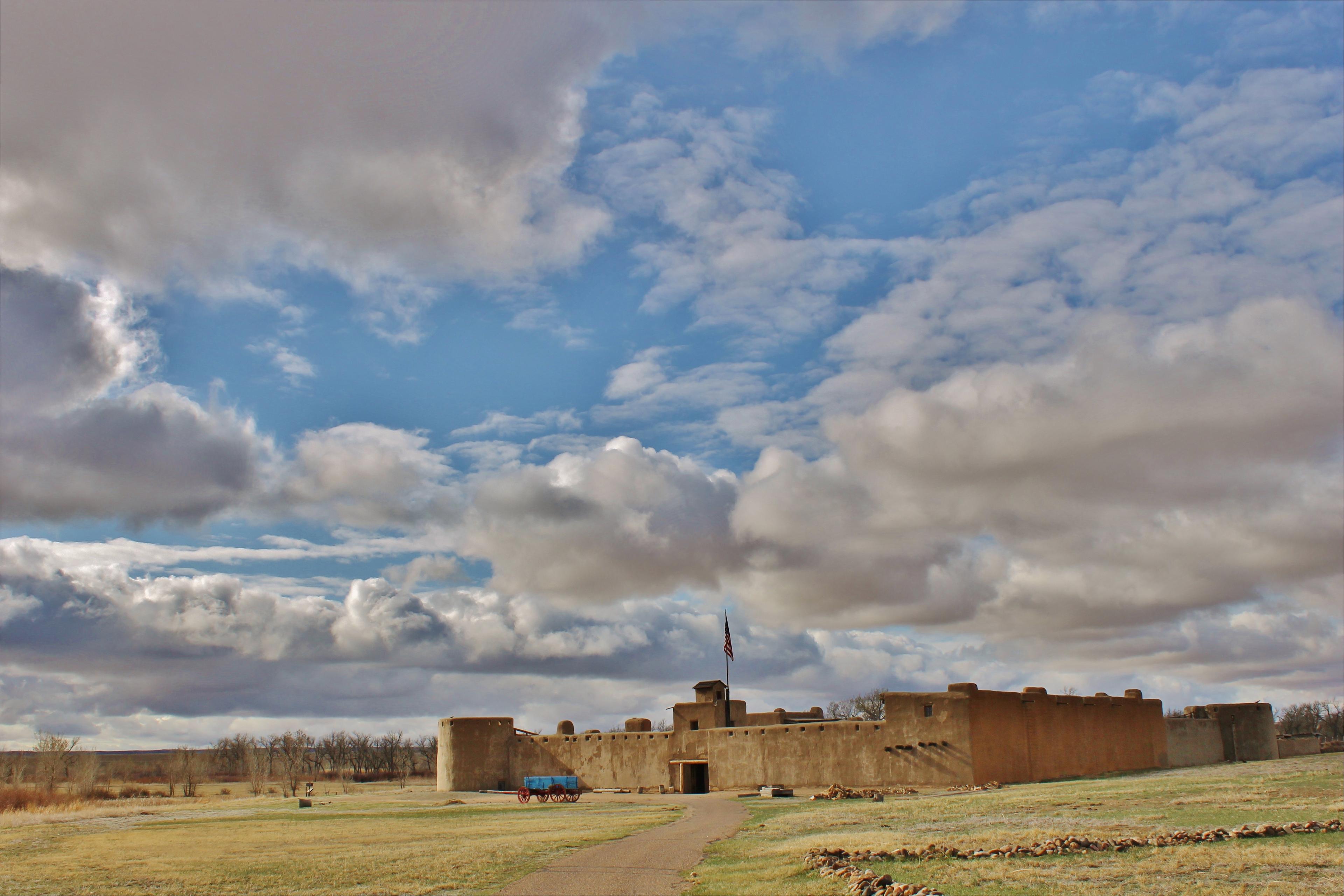 Bent's Old Fort with shortgrass prairie in foreground and blue sky and clouds above