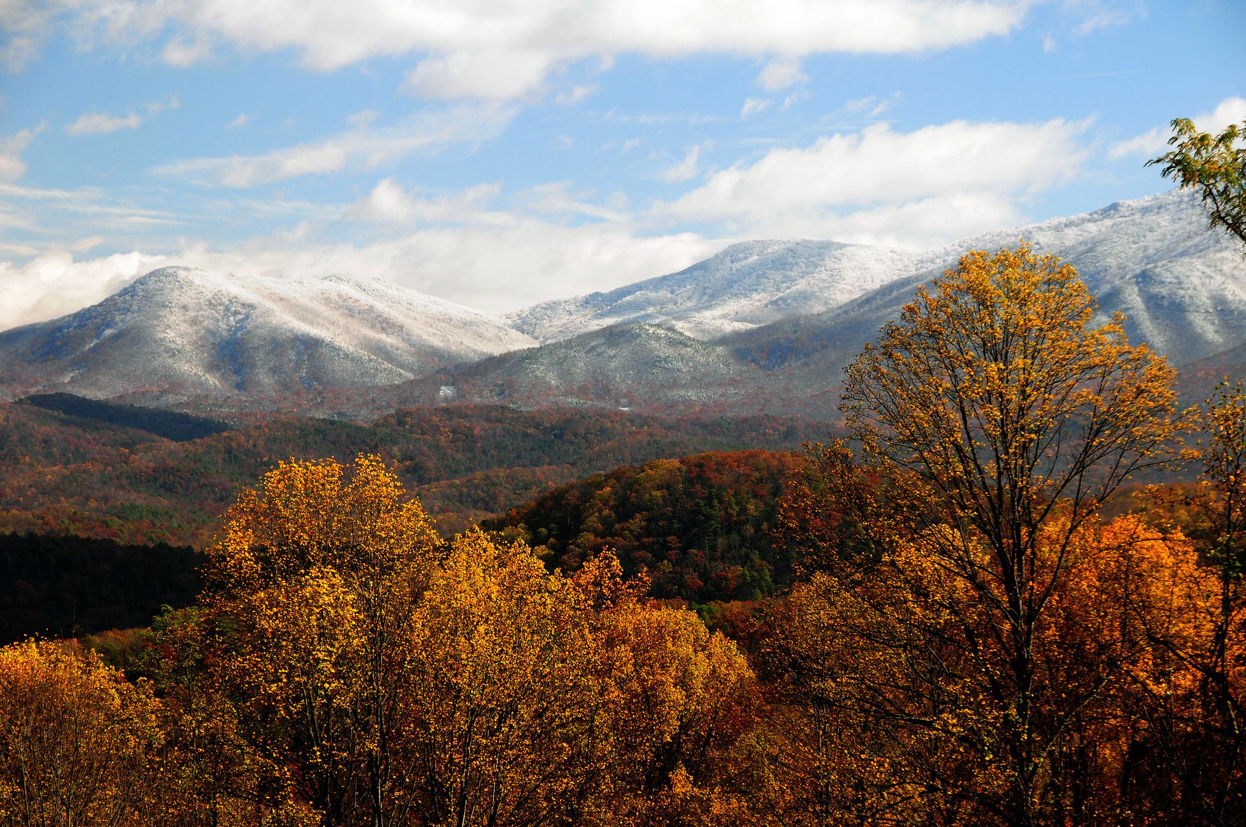 Gold and red fall colors fill the valleys while snow coats the mountain tops.