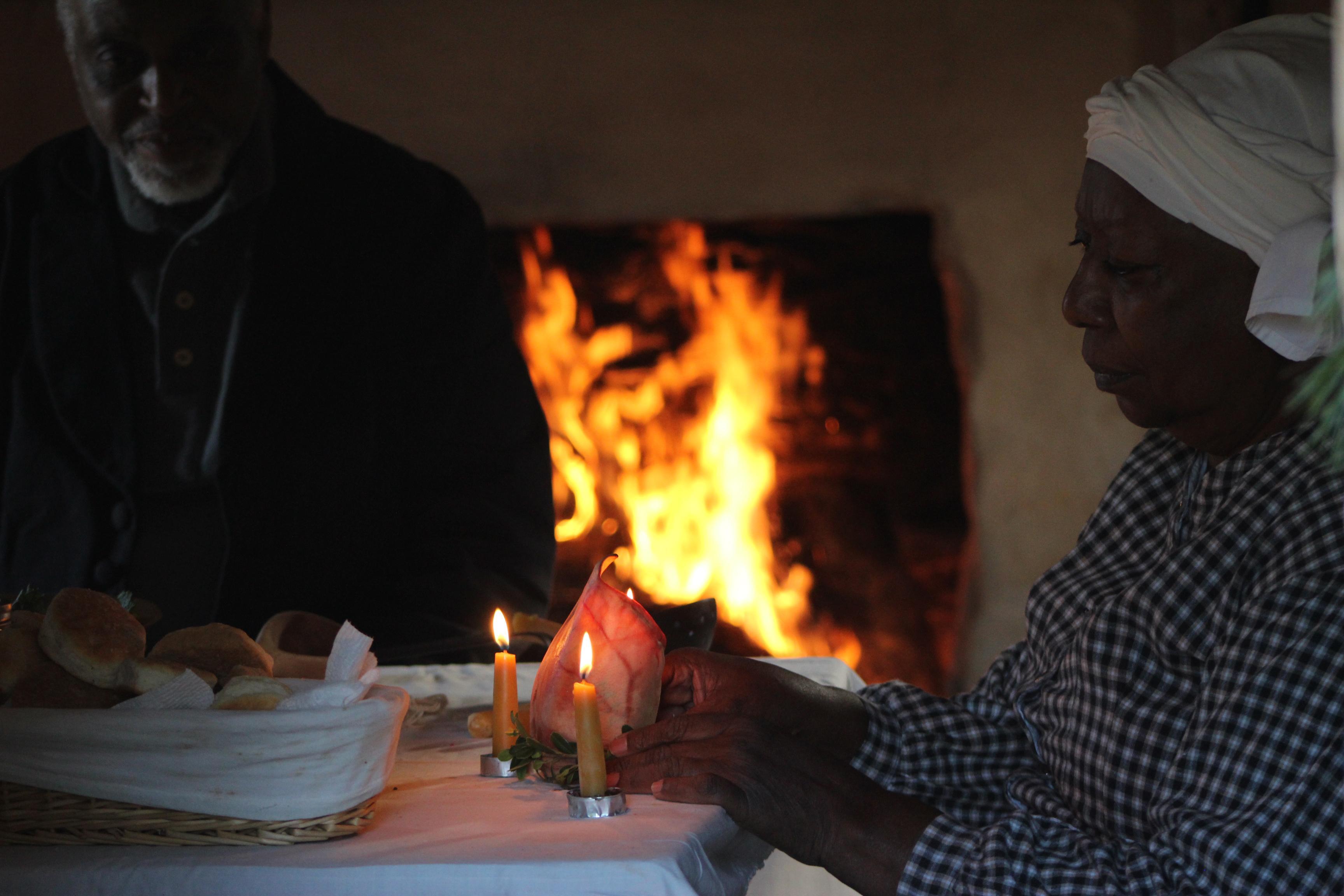 Two re-enactors portraying enslaved people sitting in front of fire inside kitchen cabin